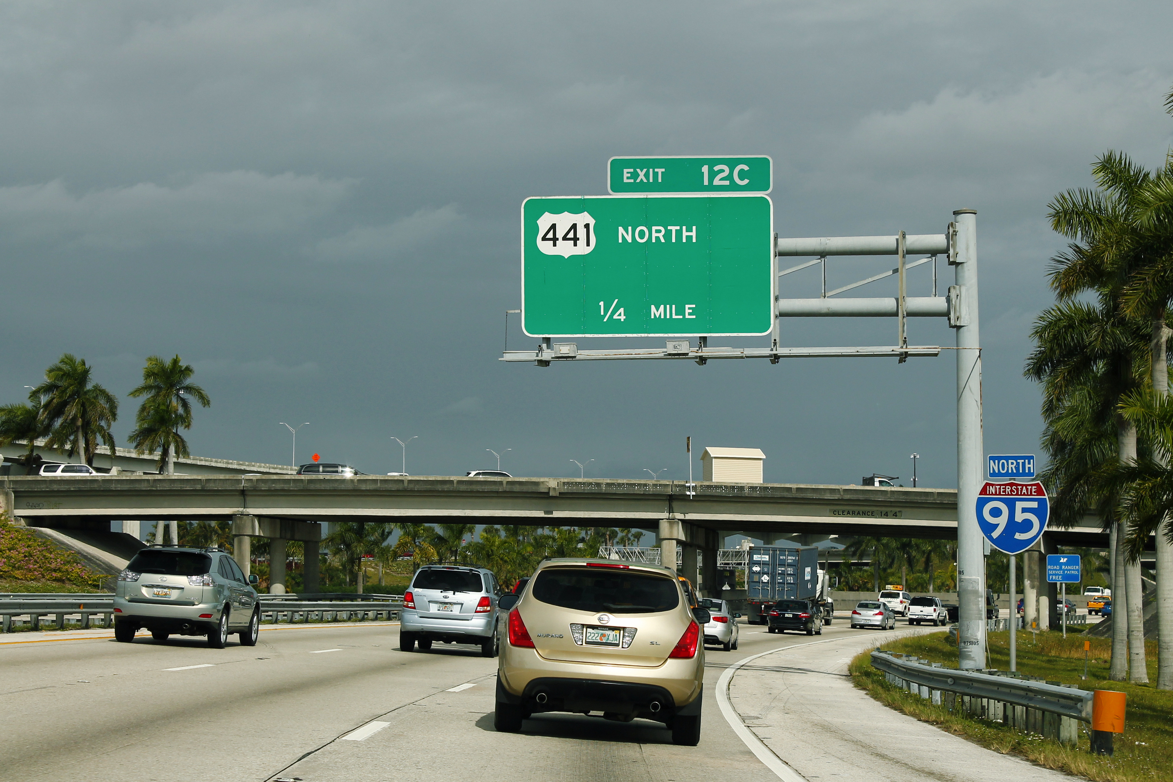 Multi-lane highway with overhead green exit sign and traffic in both directions.