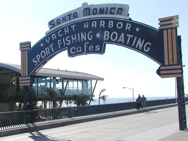 Blue arched sign spanning the entrance to the Santa Monica Pier with the ocean behind it.
