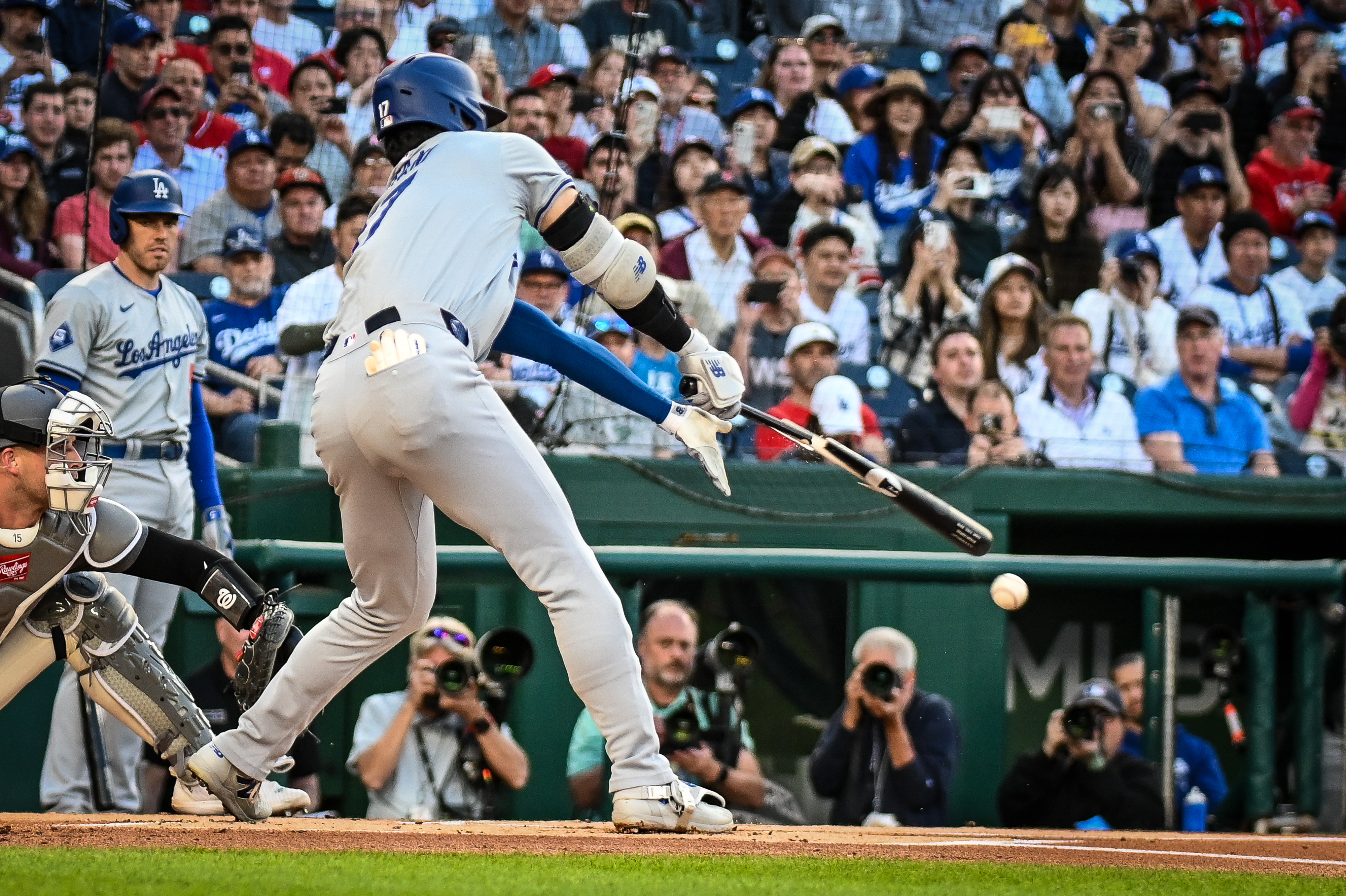 A Dodgers batter breaks his bat on contact at home plate, bat and ball visible mid-air.