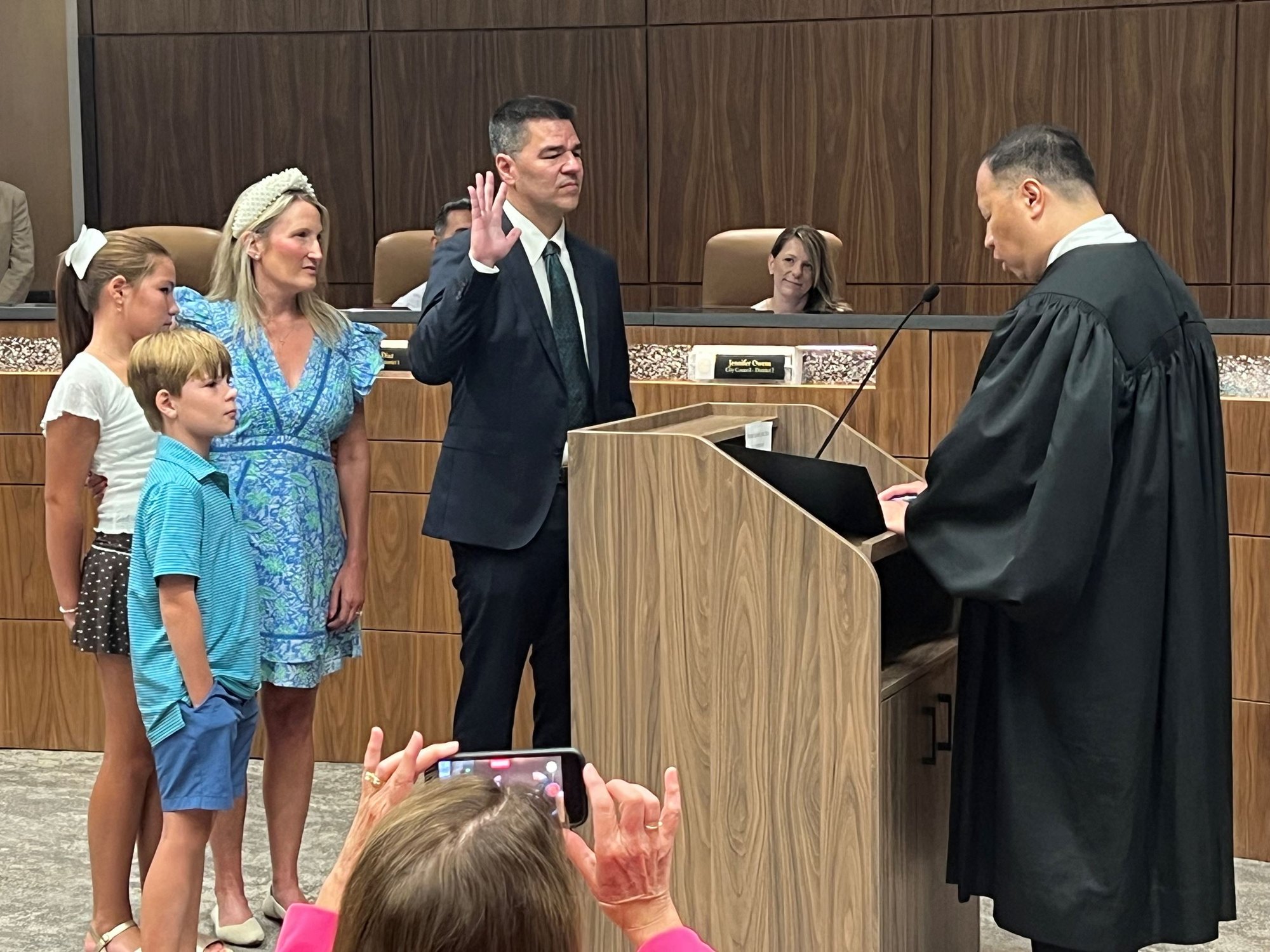 A man in a dark suit takes an oath of office at a podium while a woman and two children stand beside him.