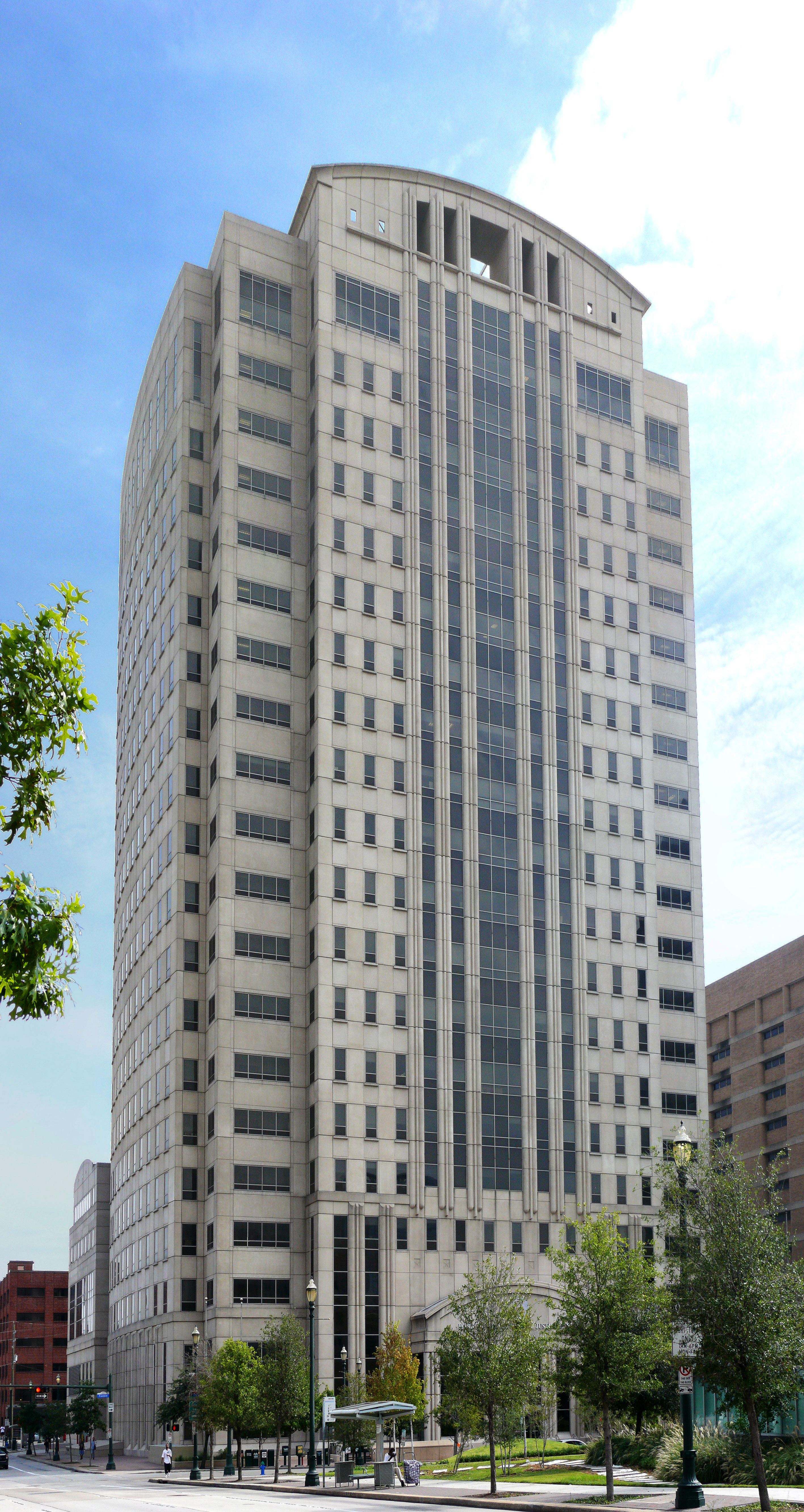 Tall courthouse tower with curved top, stone and glass facade, and street-level trees.