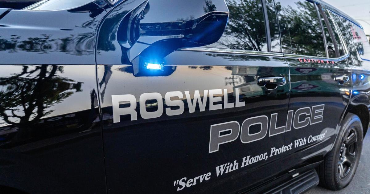 Black Roswell Police SUV with blue emergency light illuminated on the side.