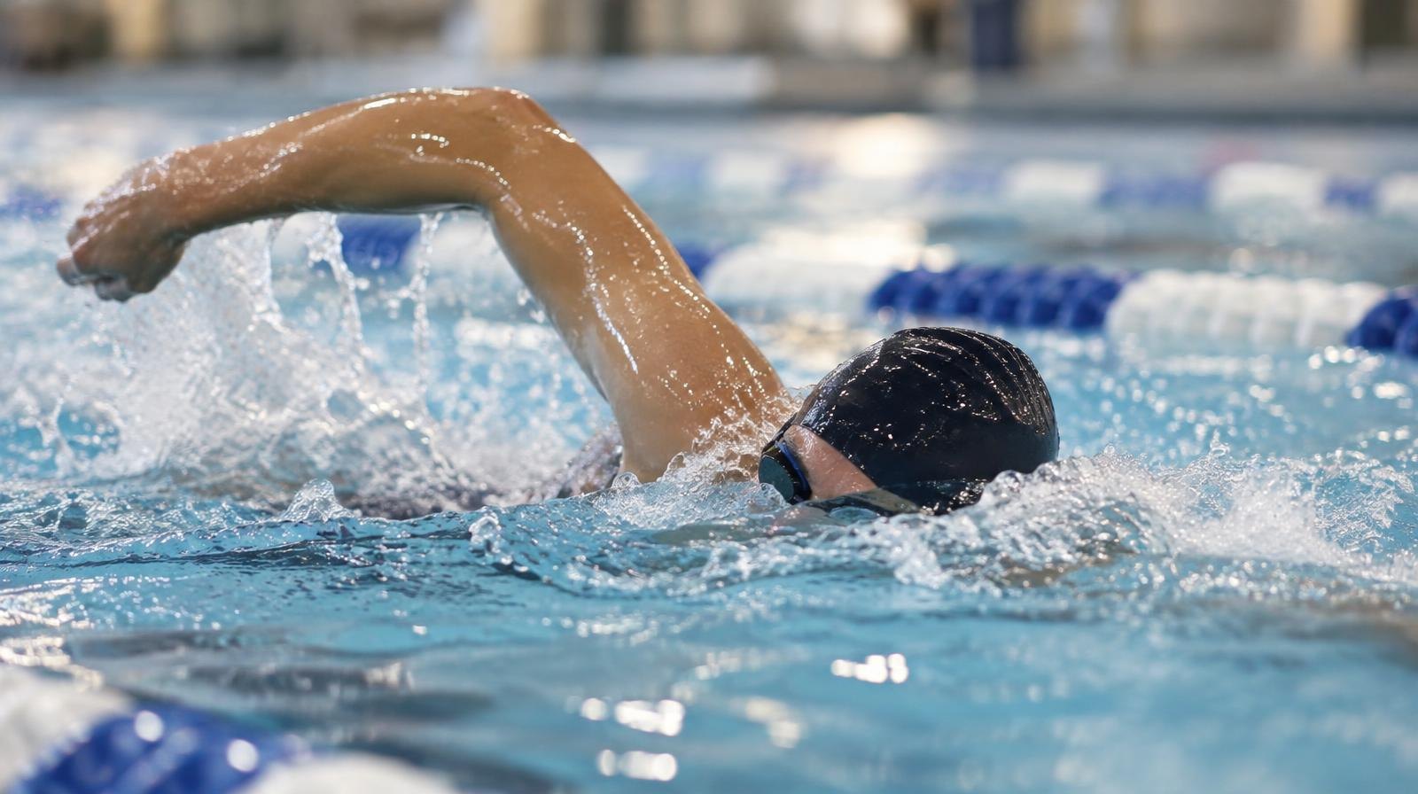 A swimmer wearing a cap and goggles mid-stroke in an indoor pool lane.