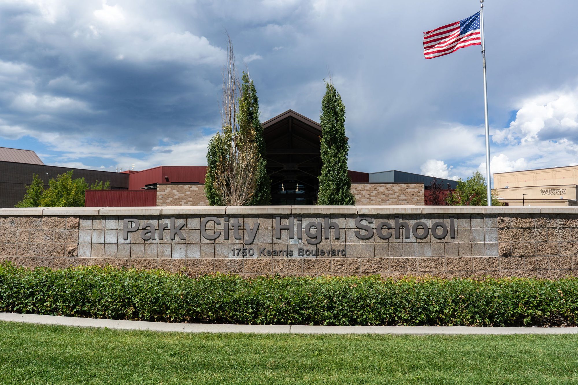 Exterior entrance of a brick high school building with a monument sign and American flag.