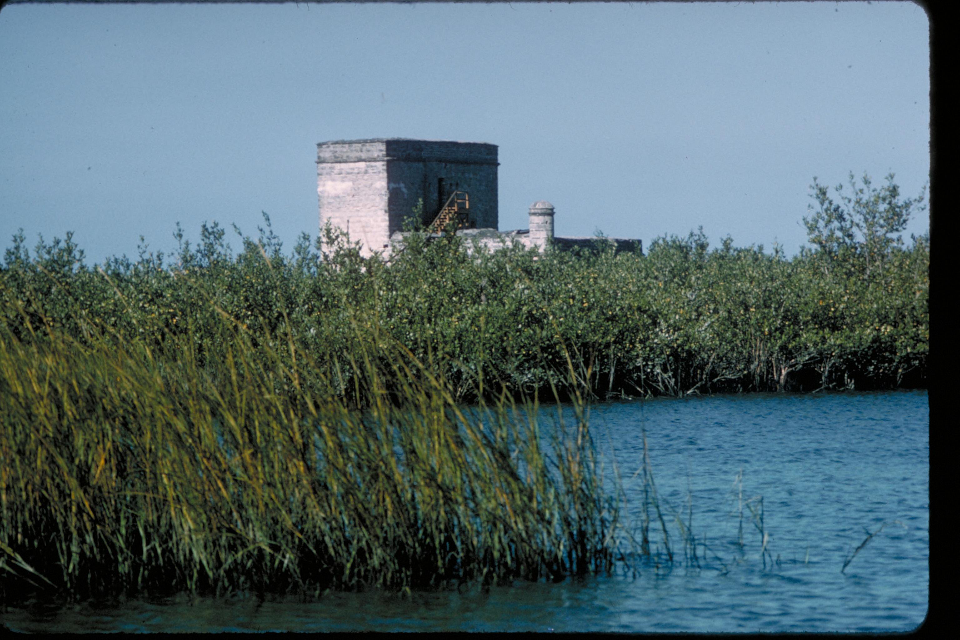 Stone fort tower visible above dense salt marsh grasses along a calm Florida estuary.
