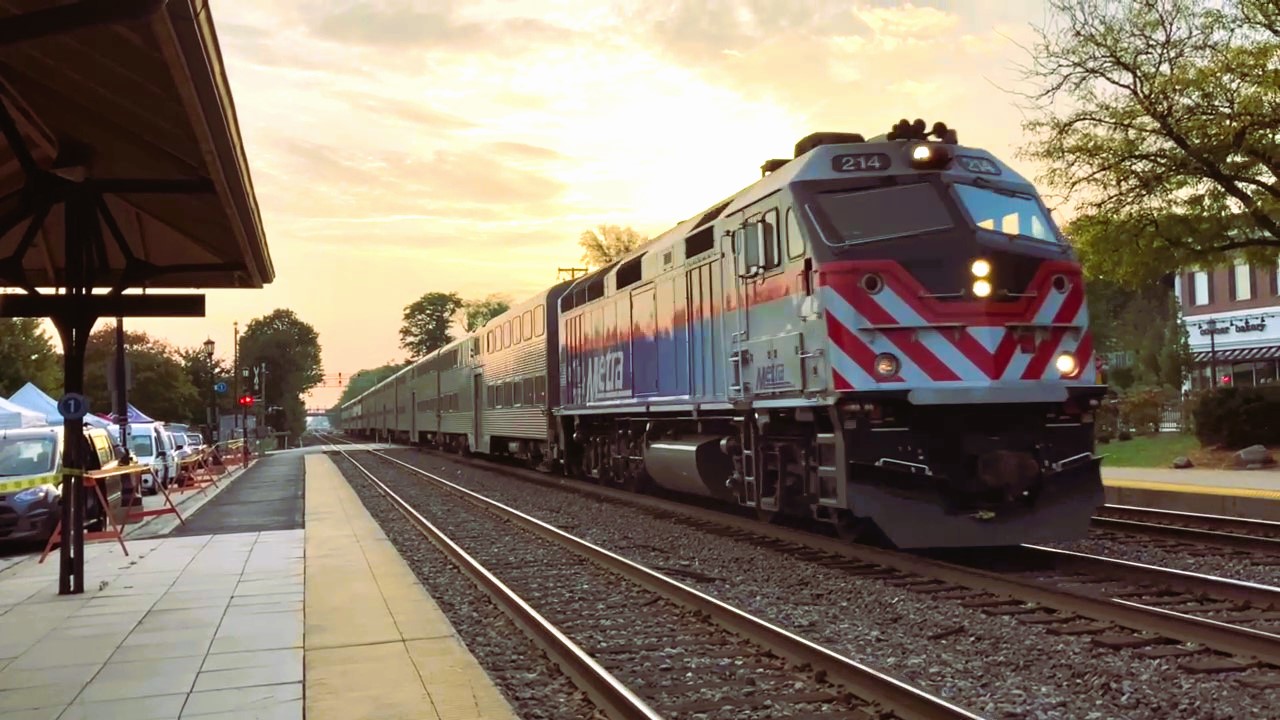 A Metra passenger train passes through a station platform at golden hour.