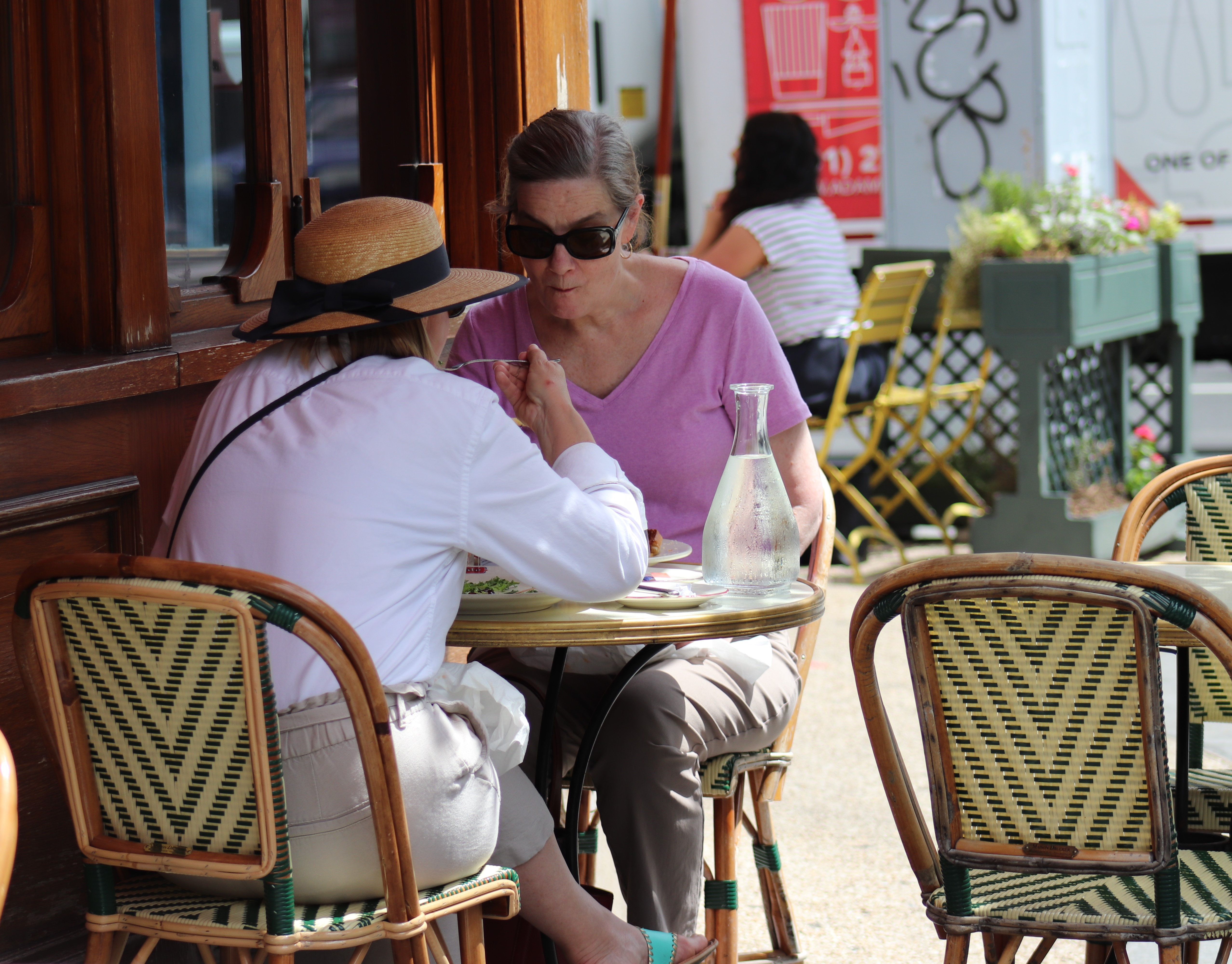 Two women seated at a small round table on an outdoor restaurant patio.