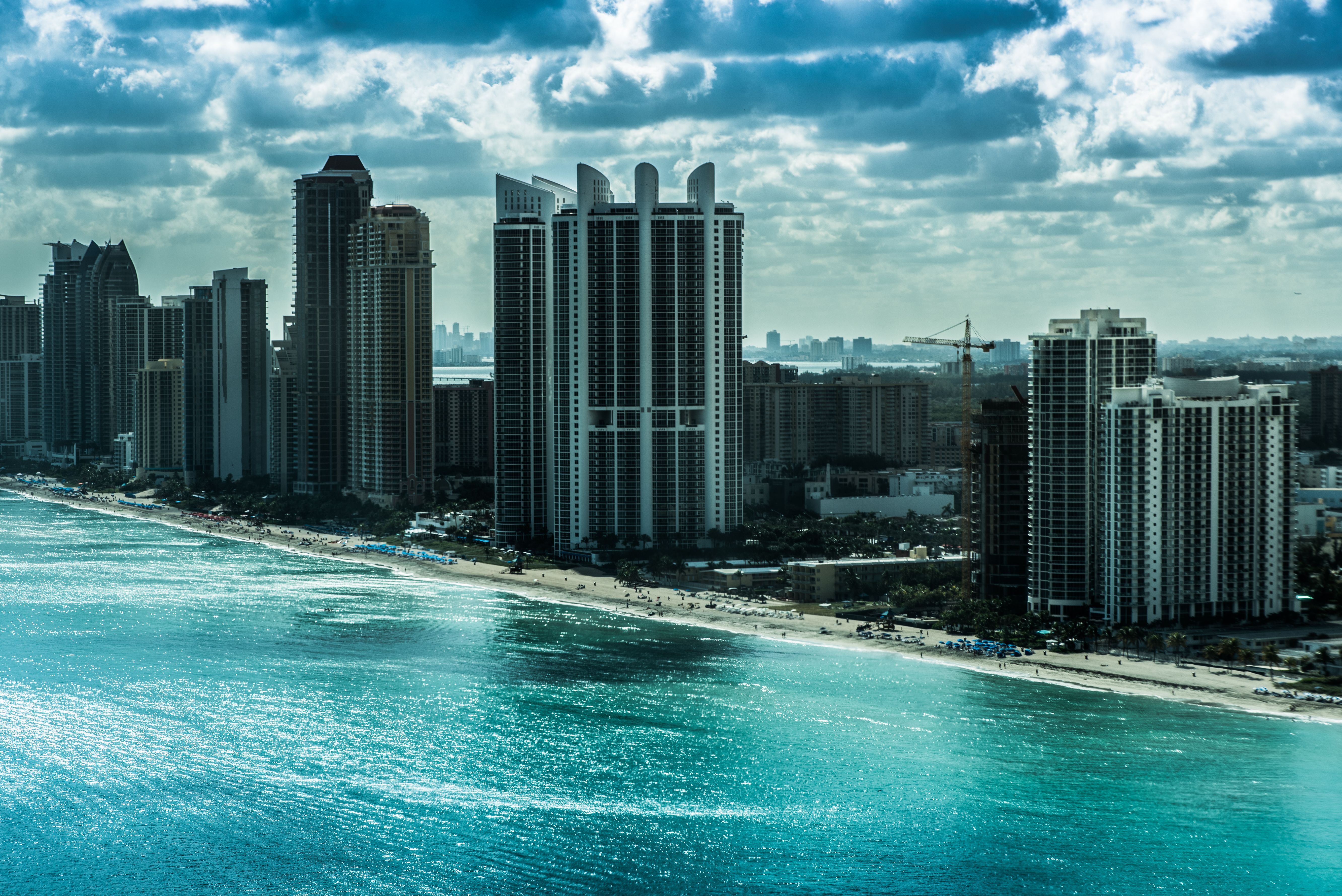 Aerial view of tall condominium towers lining a sandy beachfront under a partly cloudy sky.