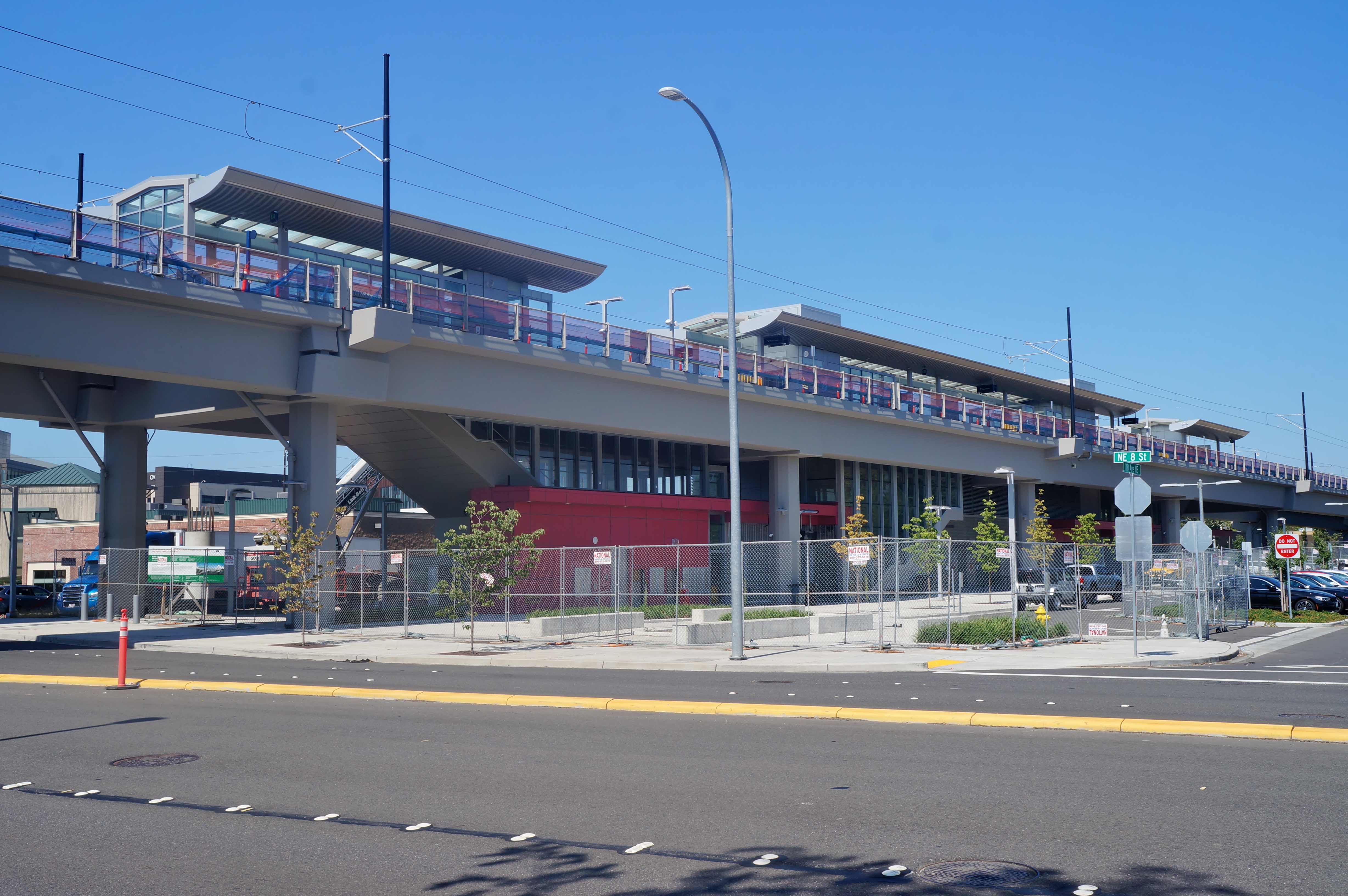 An elevated light rail station under construction with concrete columns and a glass-and-metal facade.