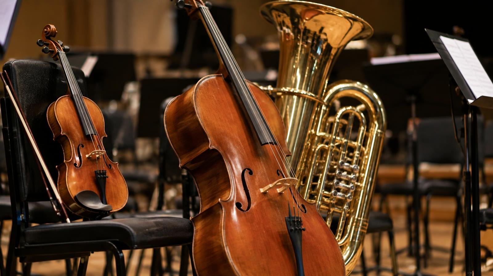 A violin, cello, and tuba arranged together on a warmly lit concert stage.