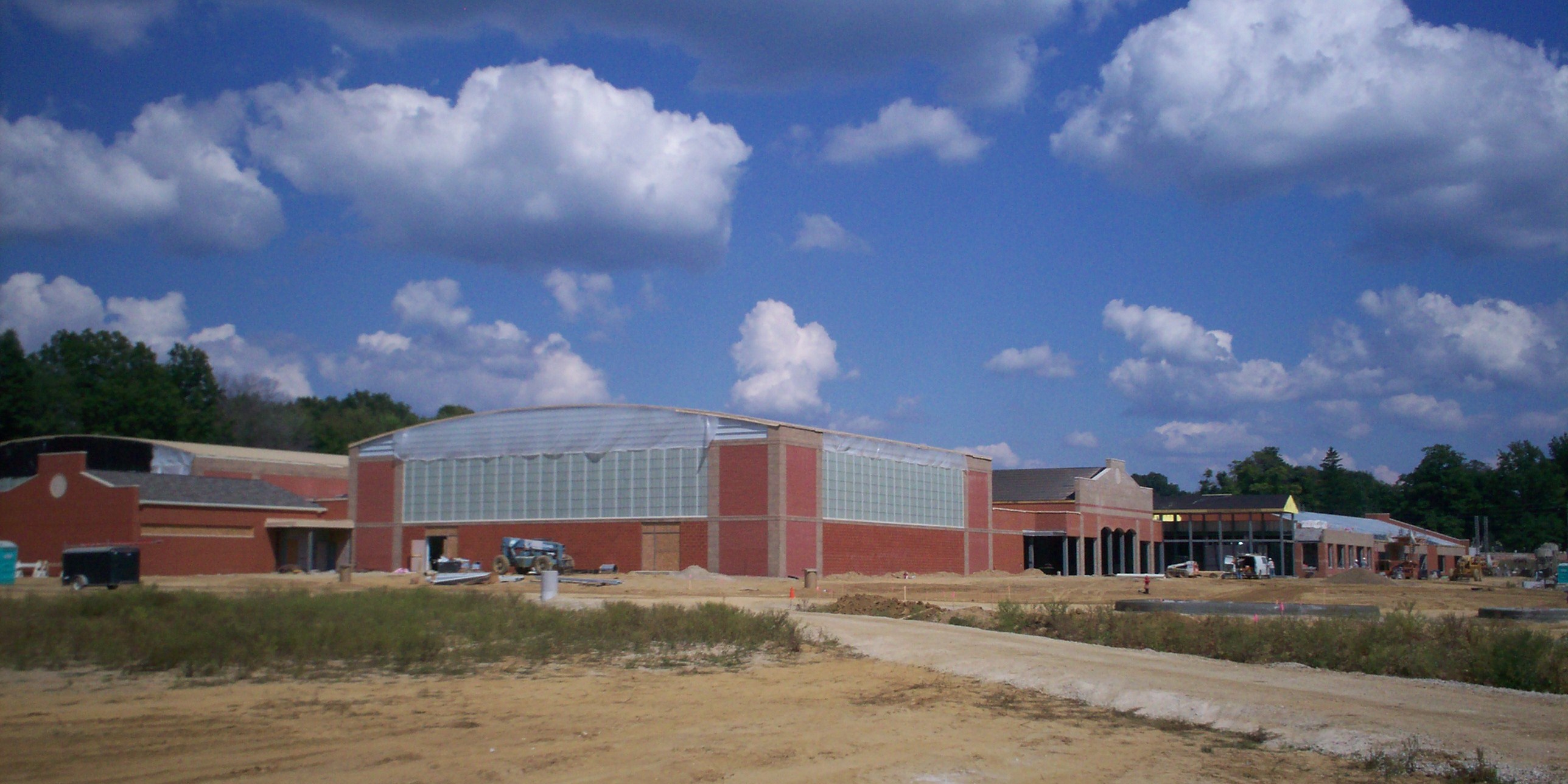 Large brick school building under construction with bare dirt grounds and equipment nearby.