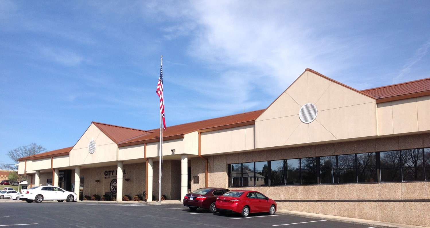 Single-story tan municipal building with a red metal roof and American flag.