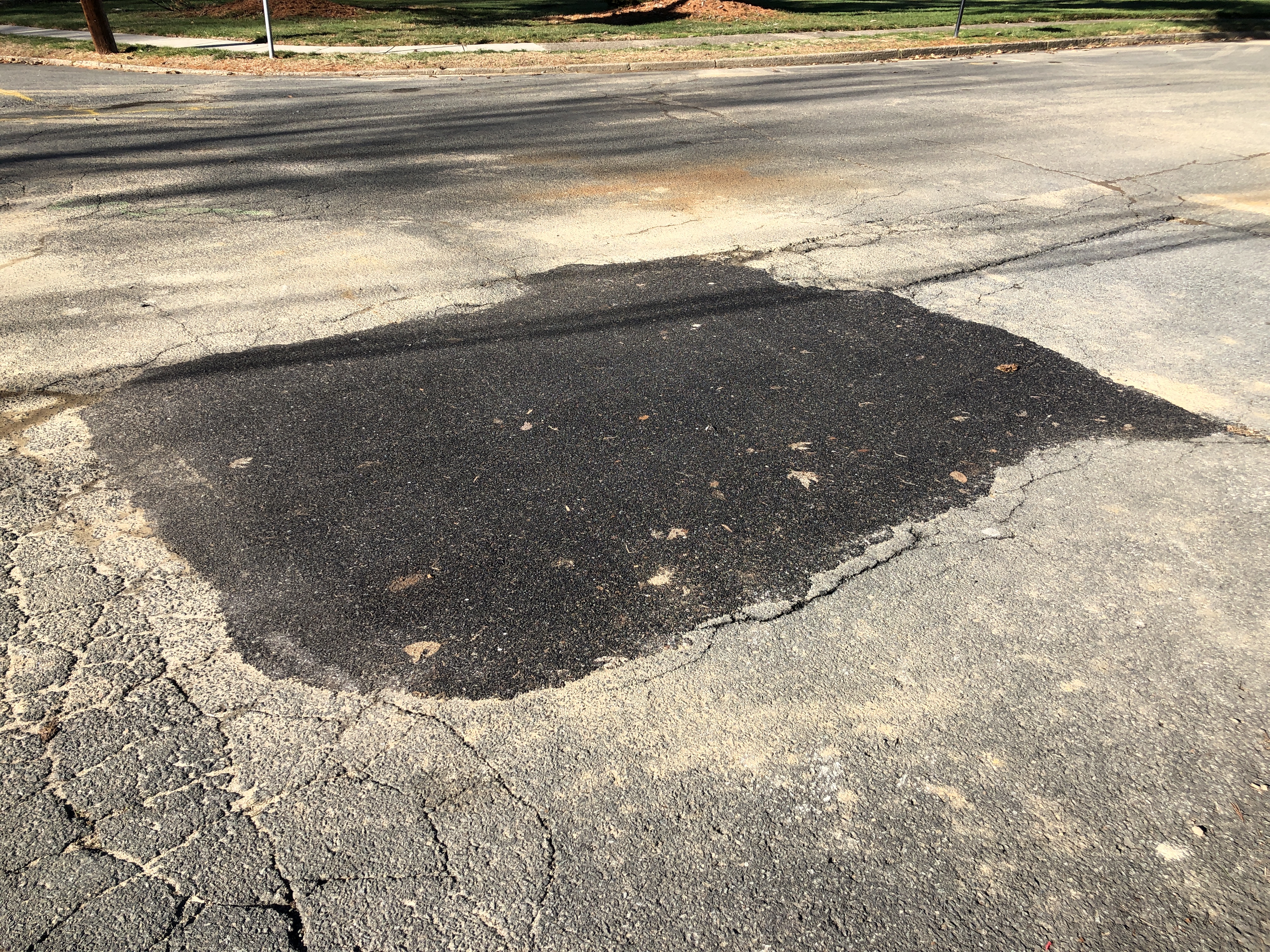 Fresh dark asphalt patch surrounded by cracked, aging road surface.
