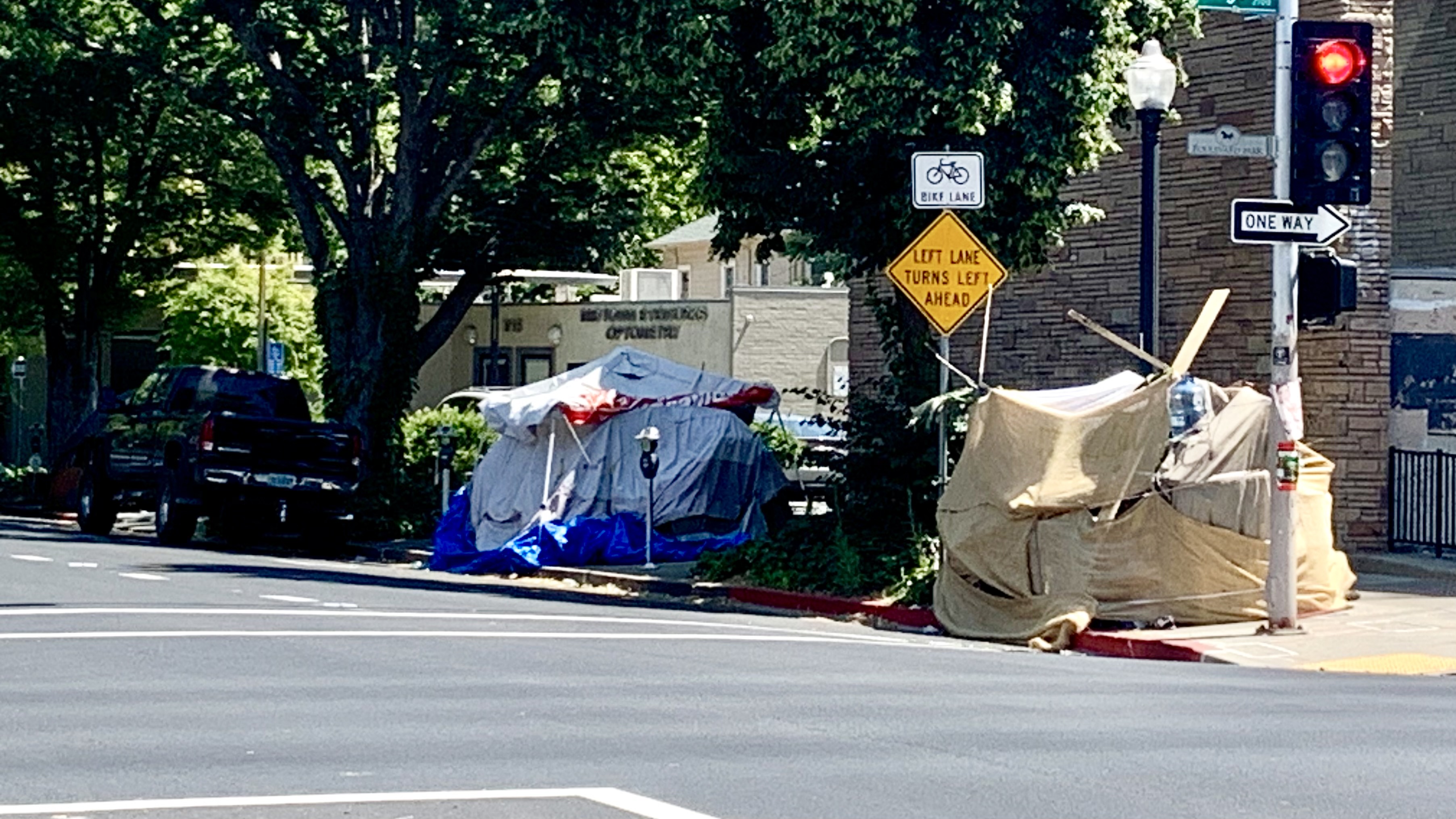Tents and tarps forming a homeless encampment on a city sidewalk corner.