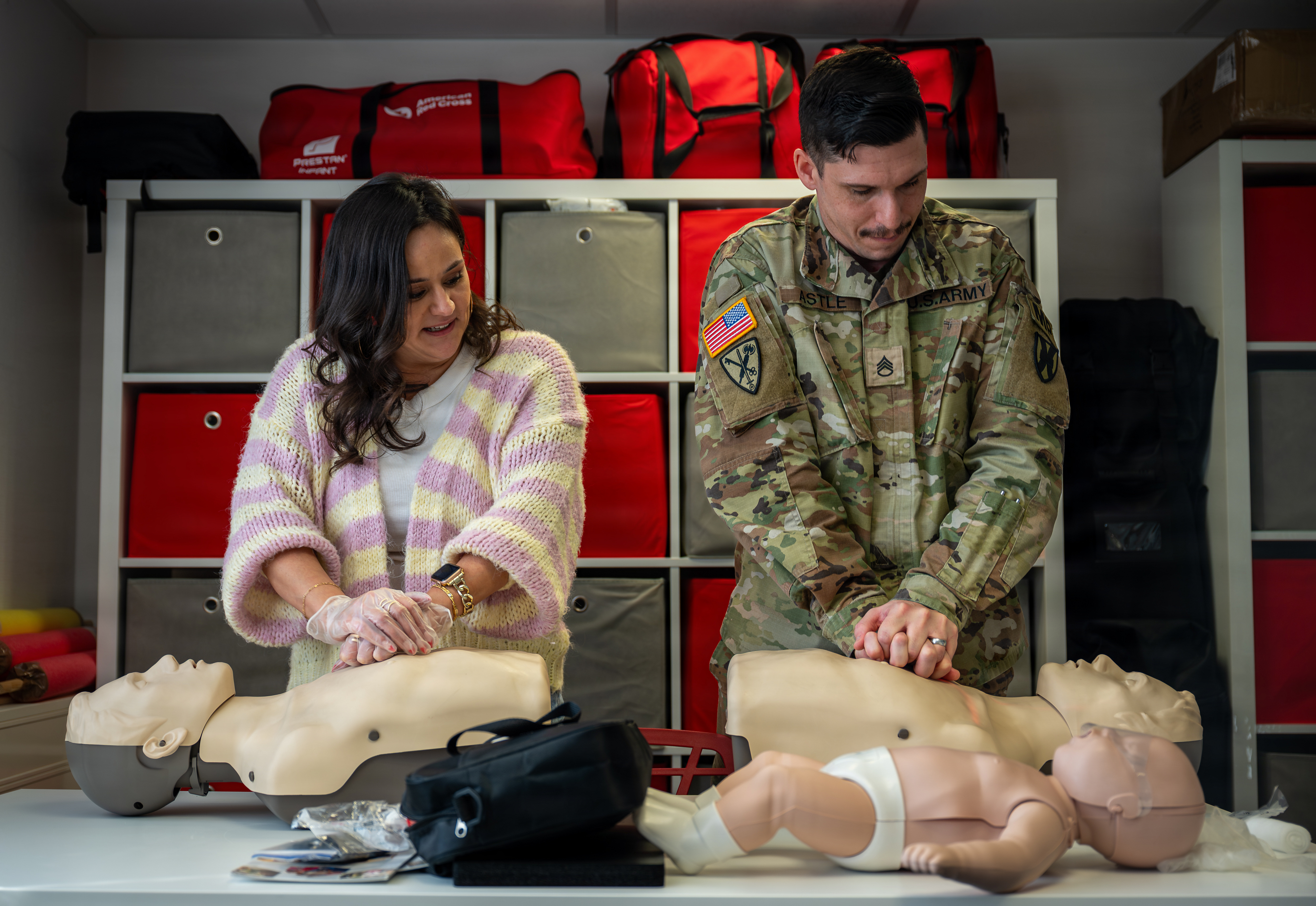 Two people perform chest compressions on adult and infant CPR training mannequins.