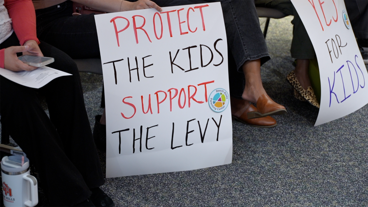 Handmade sign reading 'Protect the Kids Support the Levy' at a public gathering.
