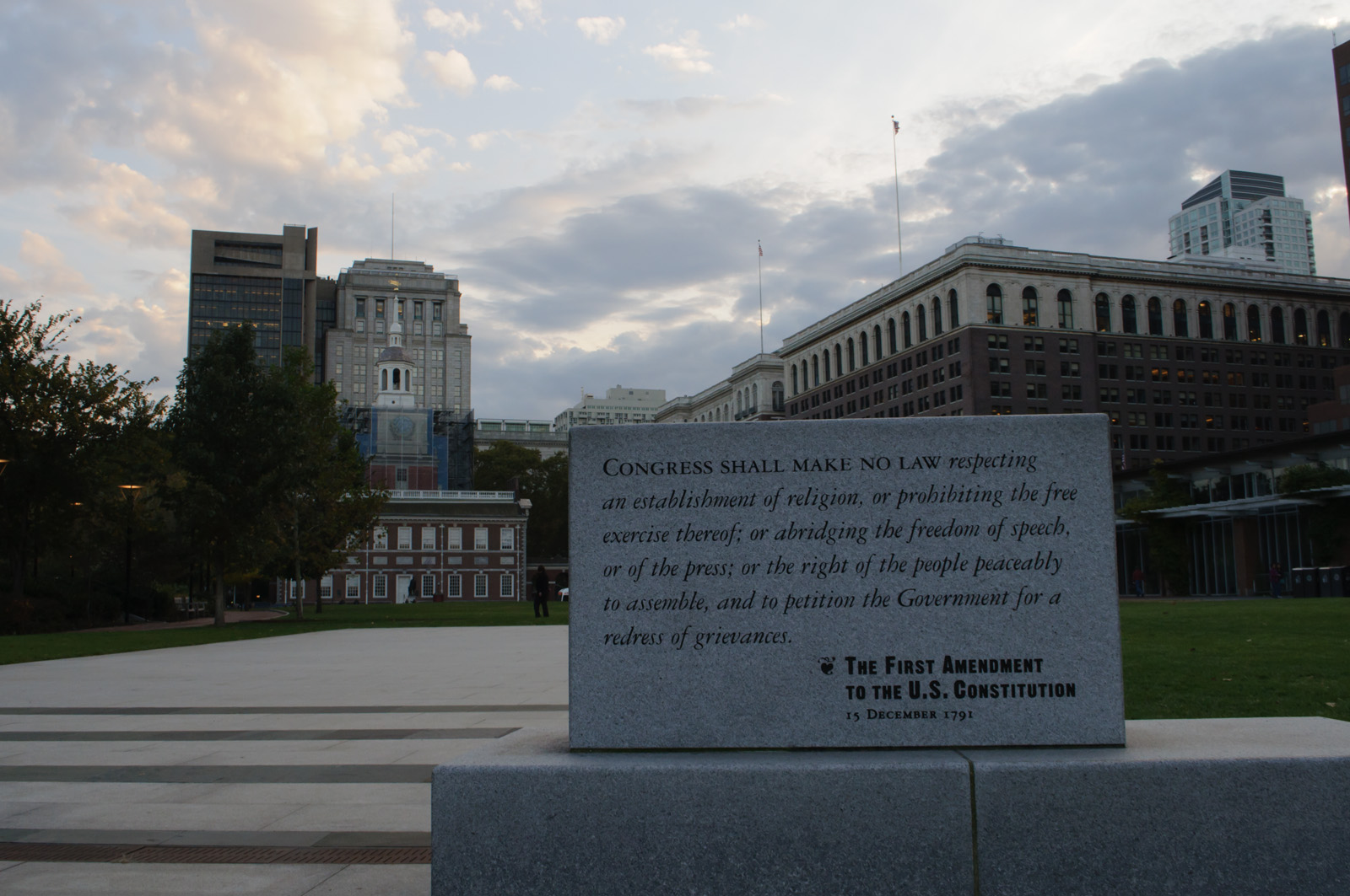 Stone monument engraved with the First Amendment text, historic building in background.