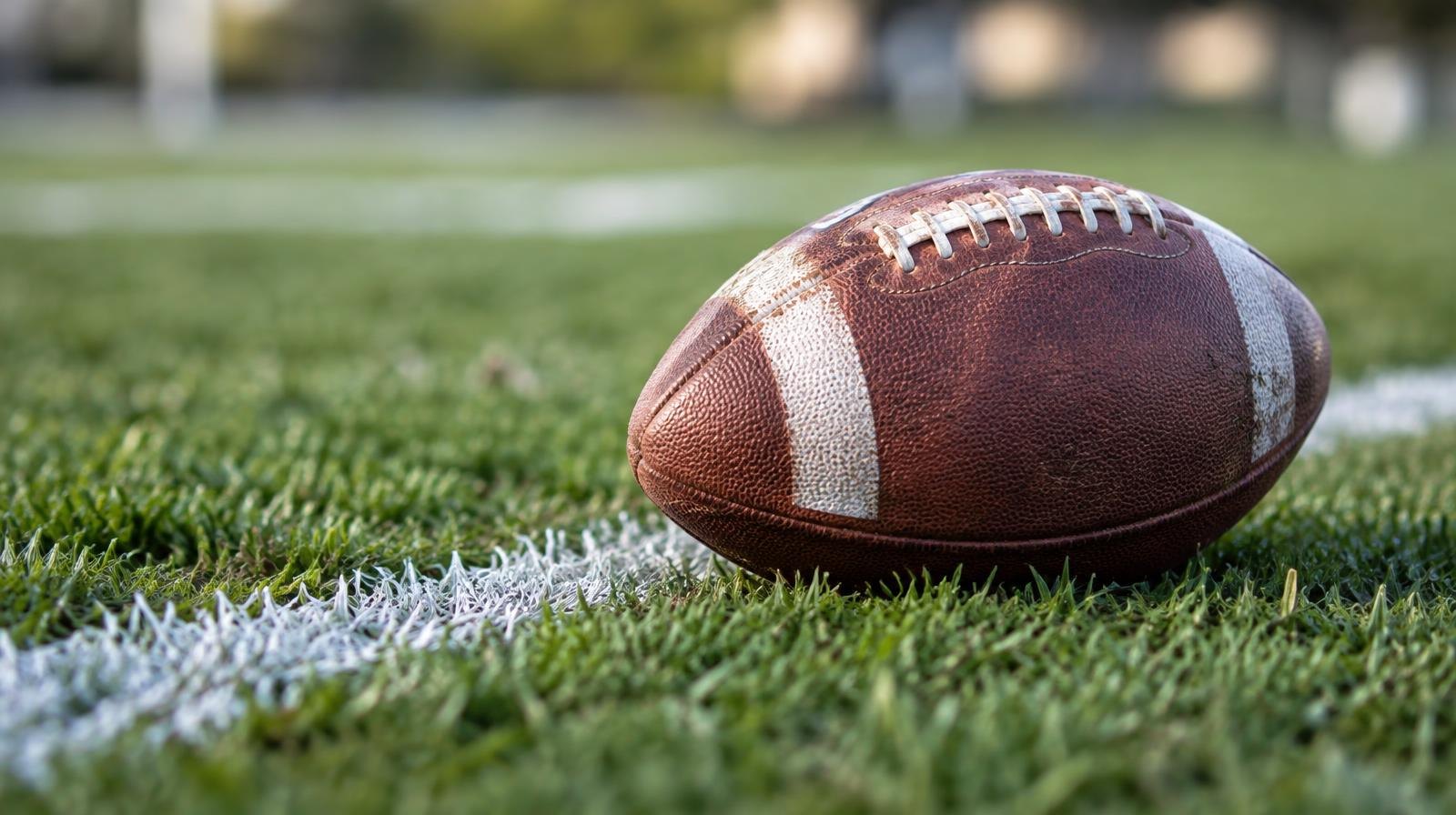 An American football resting on green grass beside a white painted yard line.