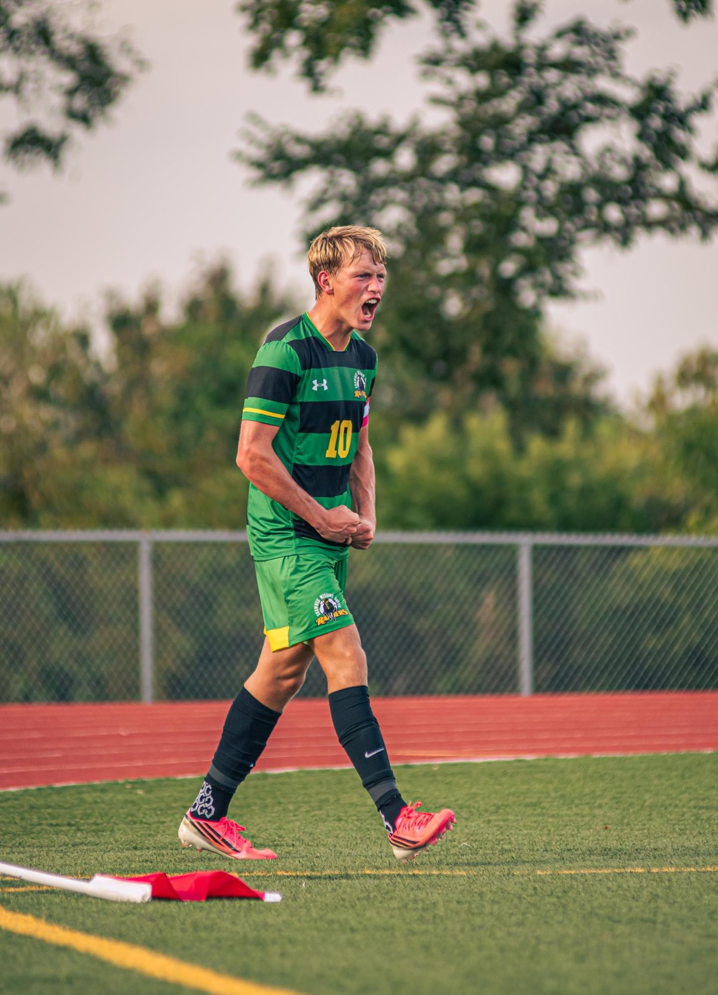 A soccer player in a green and black jersey celebrates with a fist pump on a field.