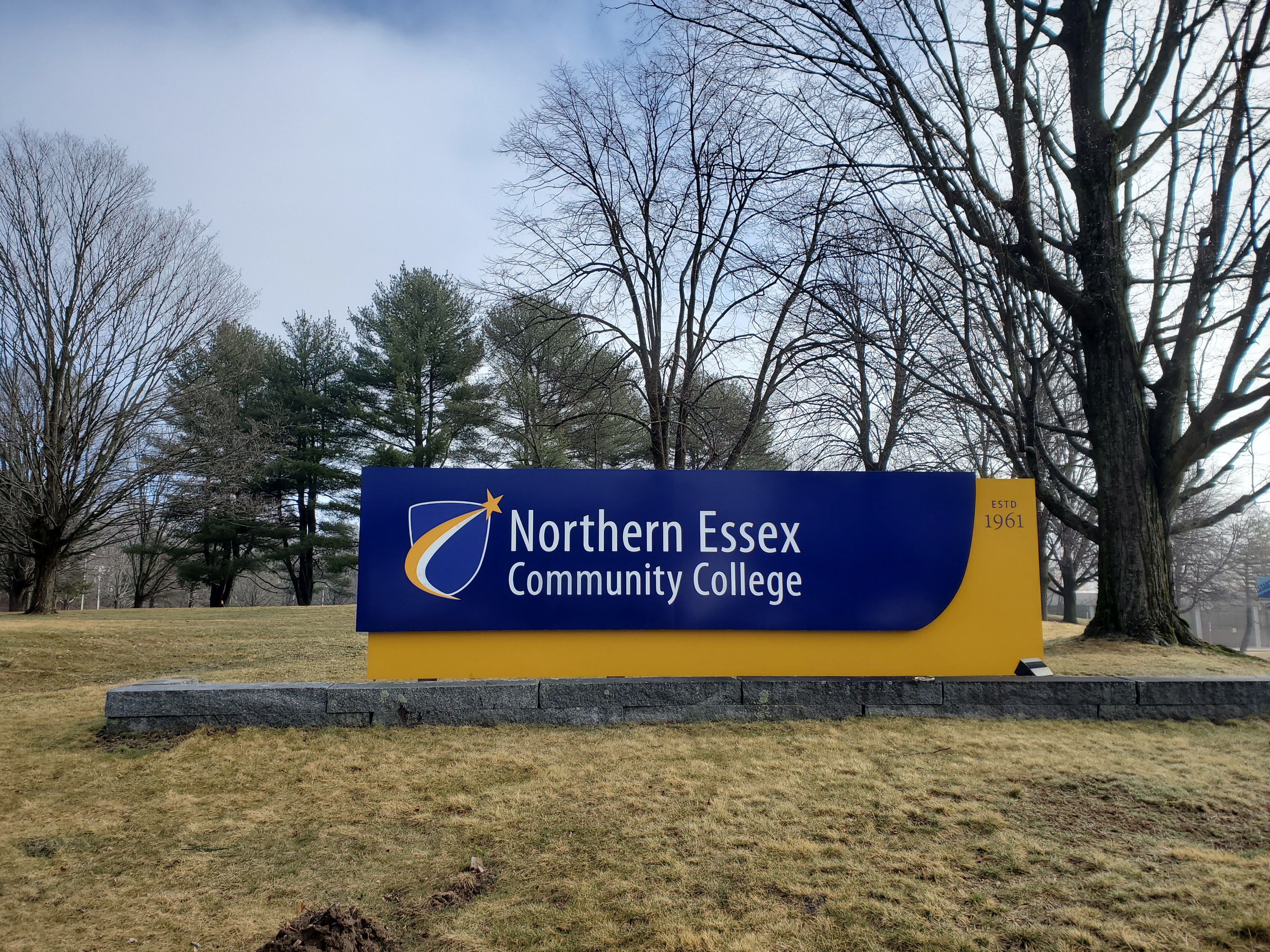 Stone-based entrance sign for Northern Essex Community College with bare winter trees behind it.