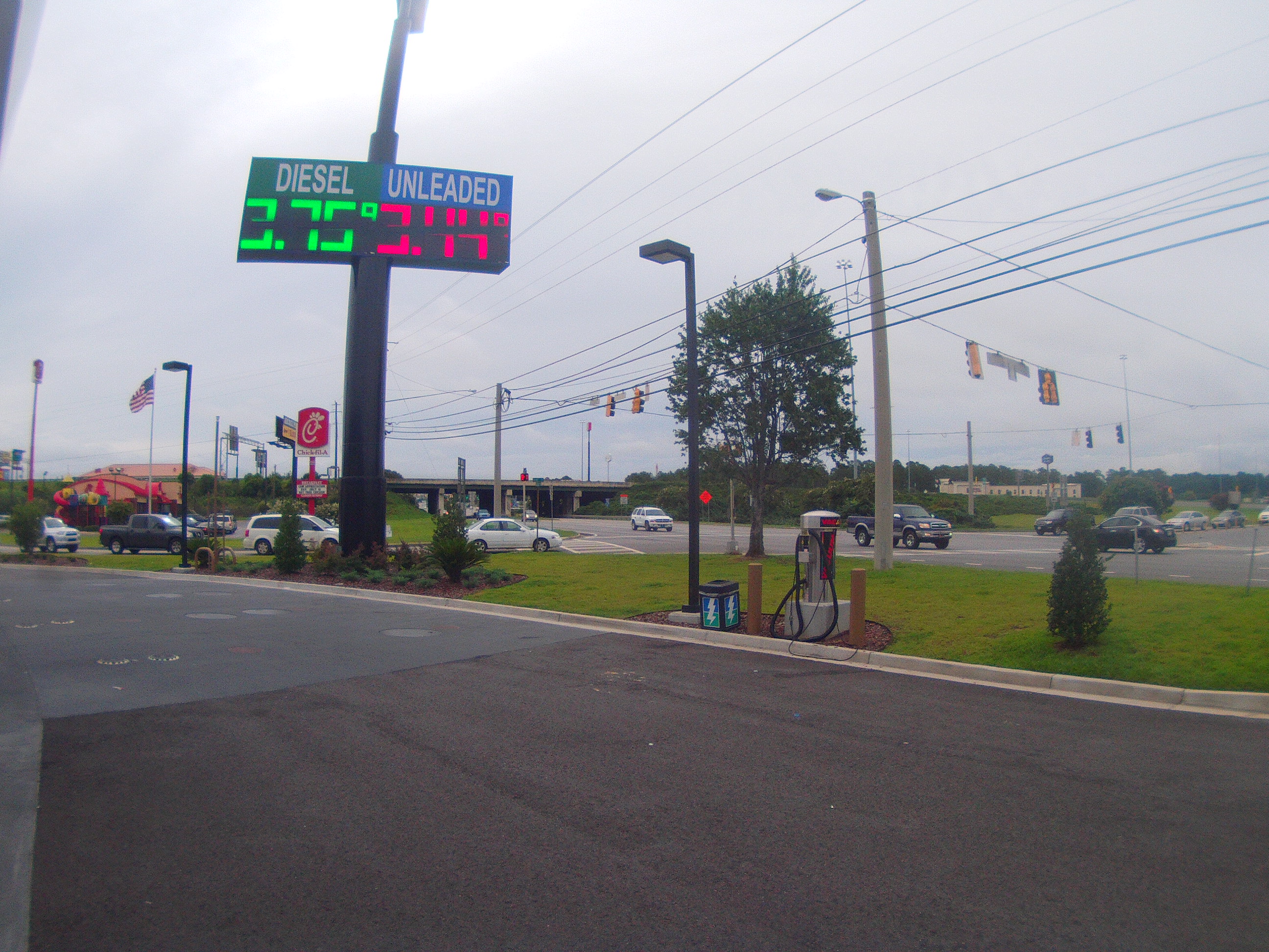 Gas station LED price sign showing diesel and unleaded fuel prices at a road intersection.