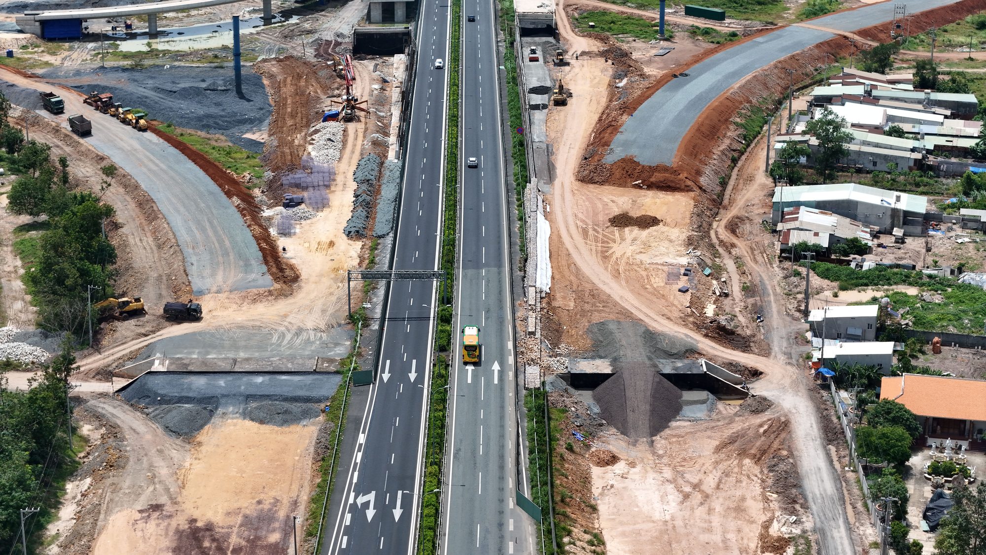 Aerial shot of highway construction with vehicles and residential area, Vietnam.