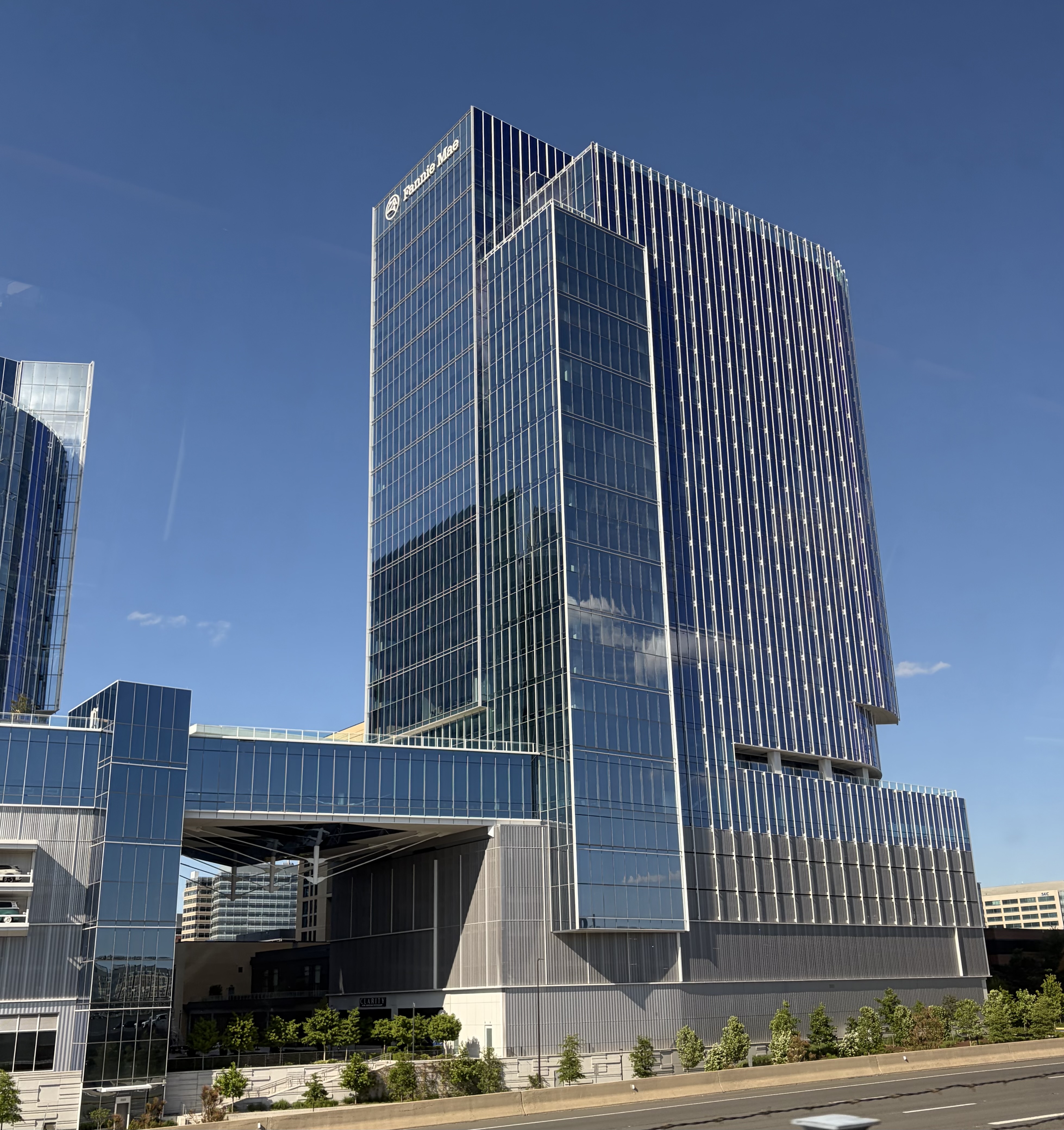 Tall glass office tower with a lower podium structure under a blue sky.