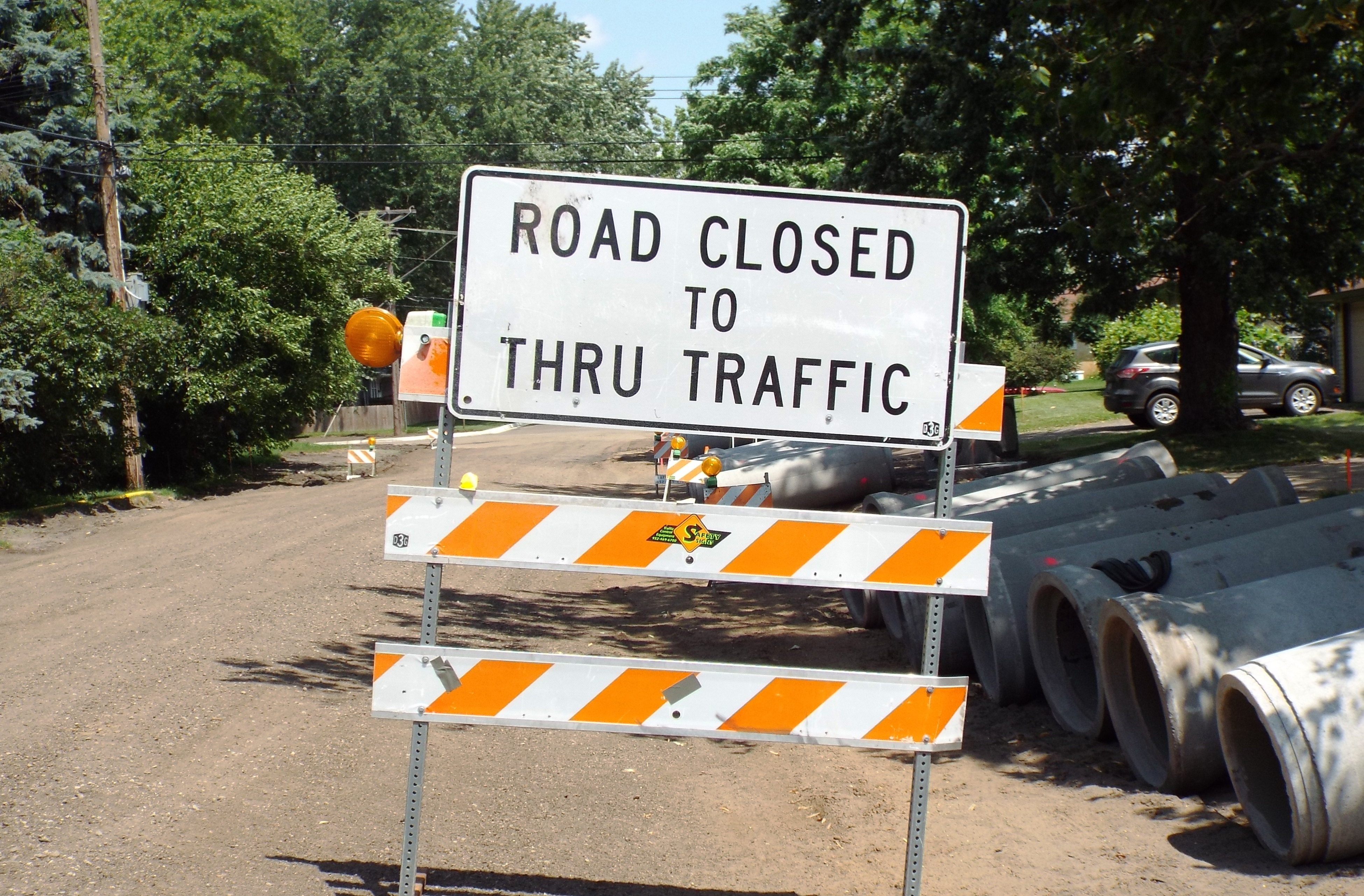 Road closed barricade sign with orange and white barriers and sewer pipes at a residential construction site.