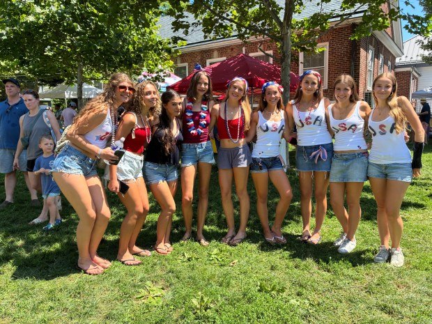 Group of young women in red, white, and blue outfits posing outdoors near a brick building.