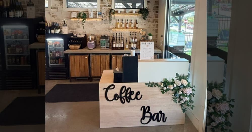 Wooden coffee bar counter with black lettering sign and white floral arrangement.