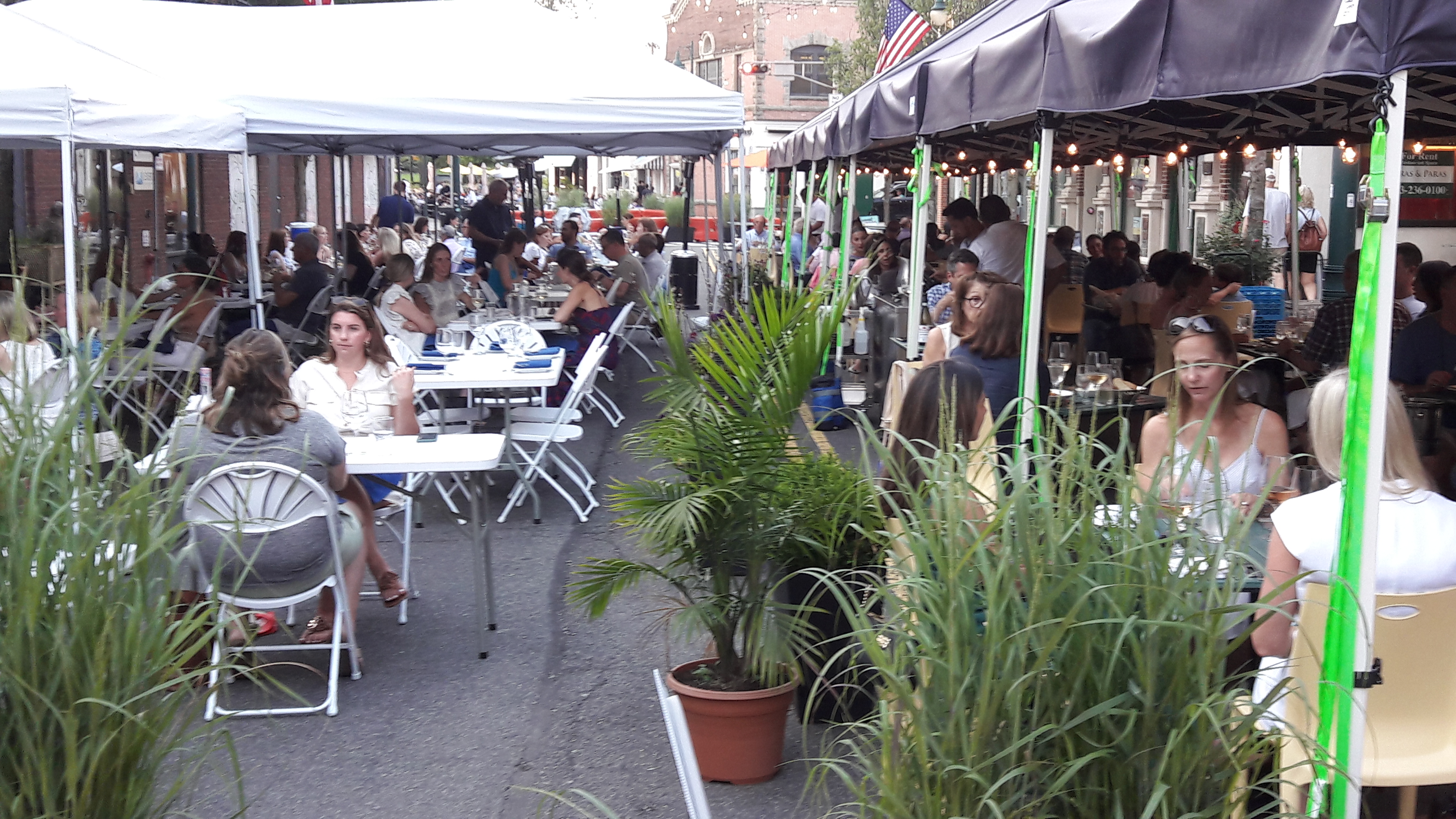 Outdoor dining tables under canopy tents on a lively downtown street at night.