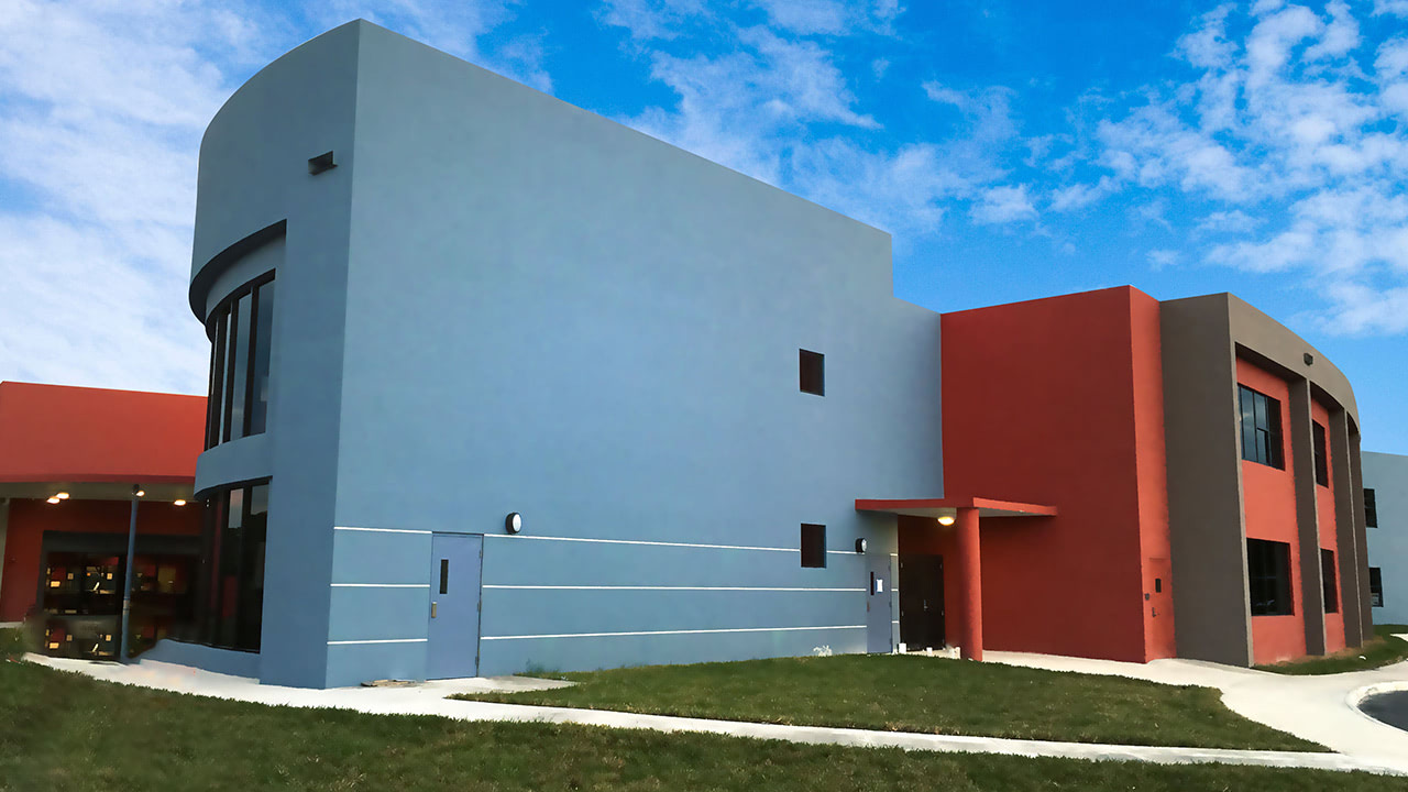 Two-story school building with blue-gray and red stucco walls and a green lawn.