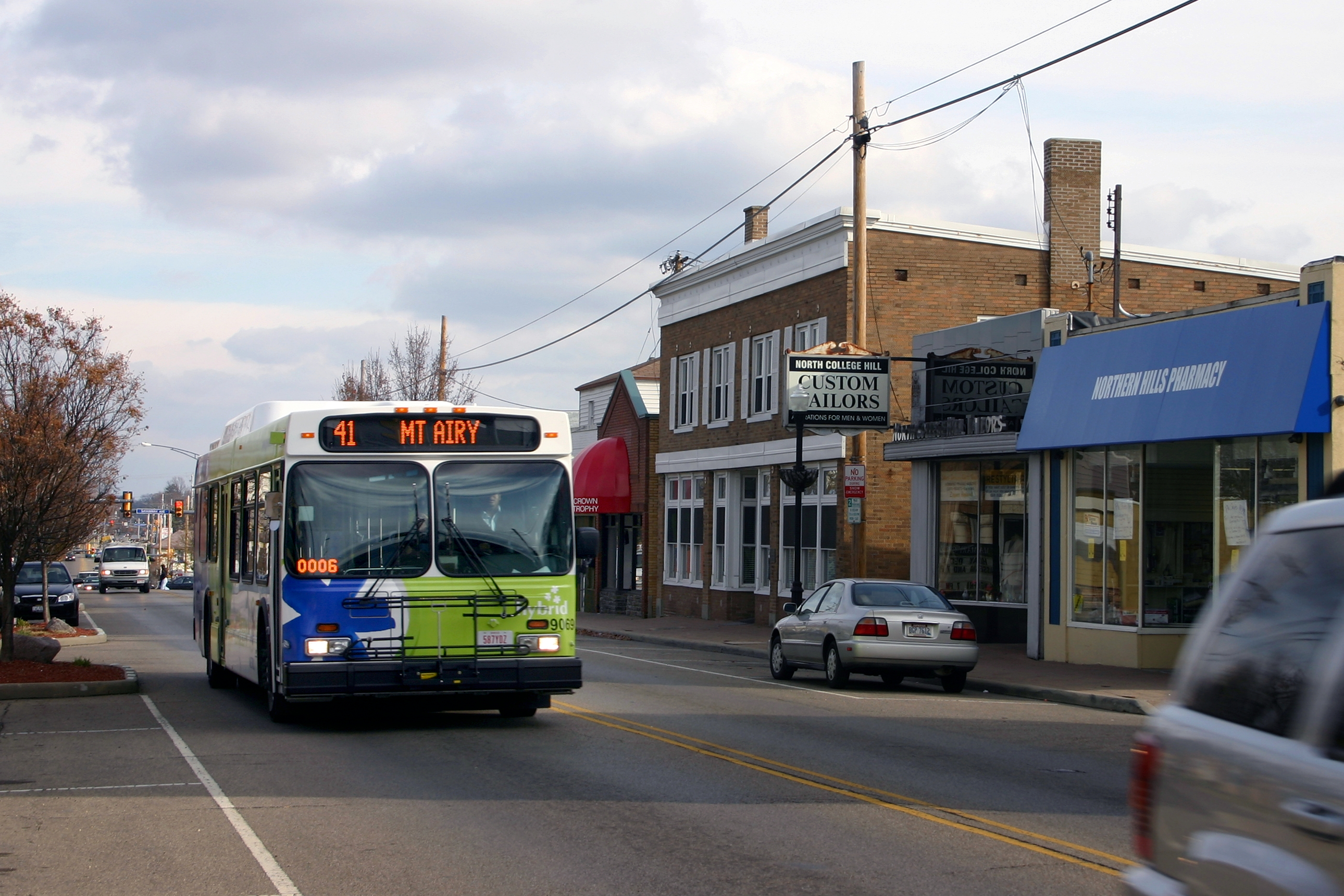 A Cincinnati Metro bus in blue and green livery travels along a commercial street.