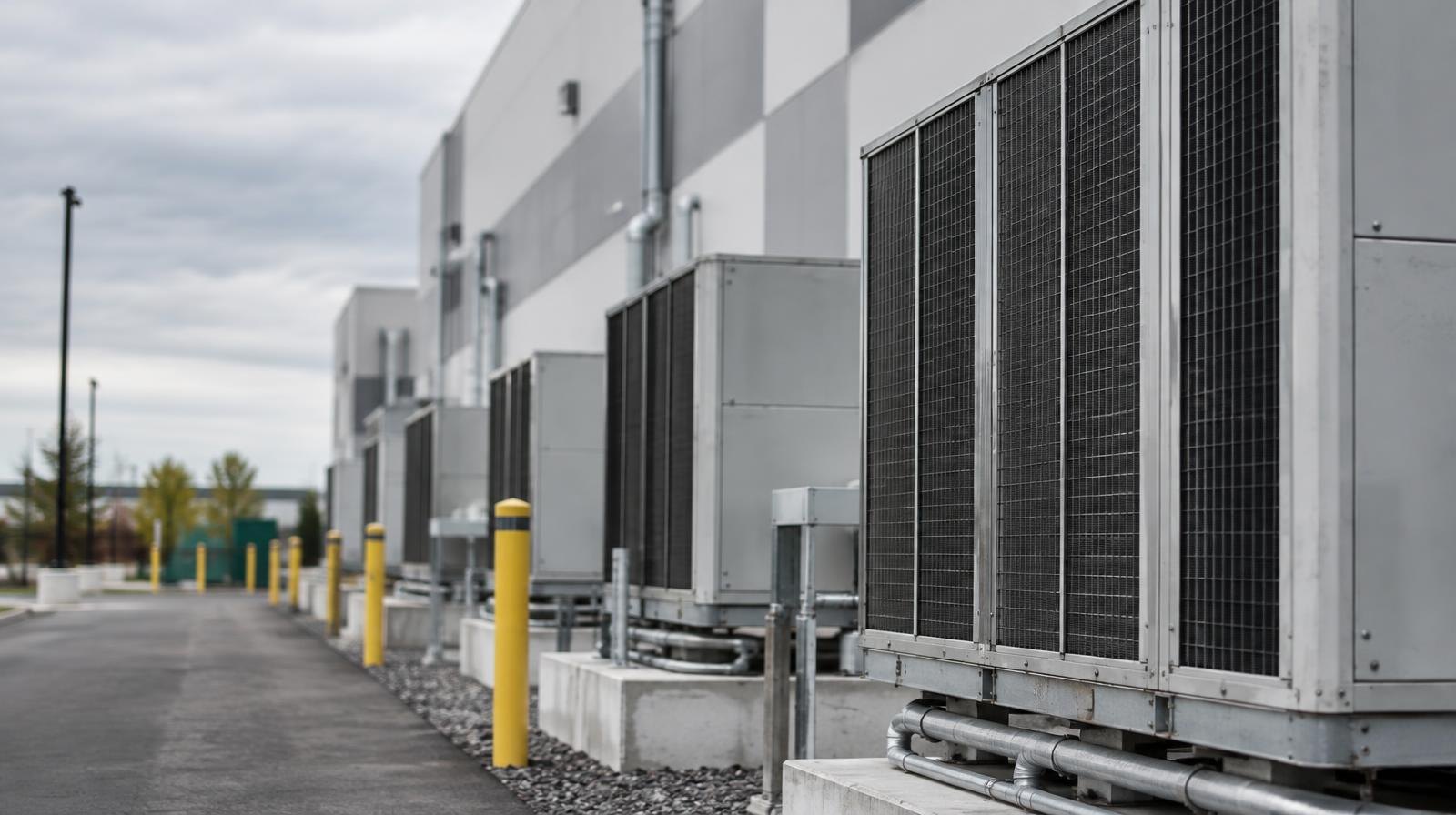 Large modern building exterior with rows of industrial cooling units along its facade.