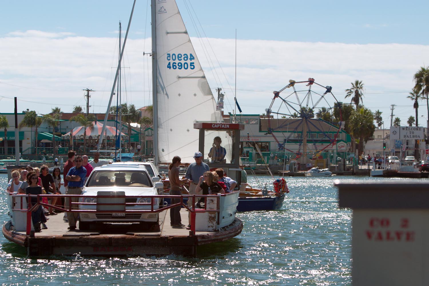 Small open-deck ferry carrying a car and passengers across a calm harbor bay.