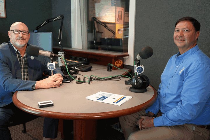 Two men seated at a podcast studio table with microphones and recording equipment.