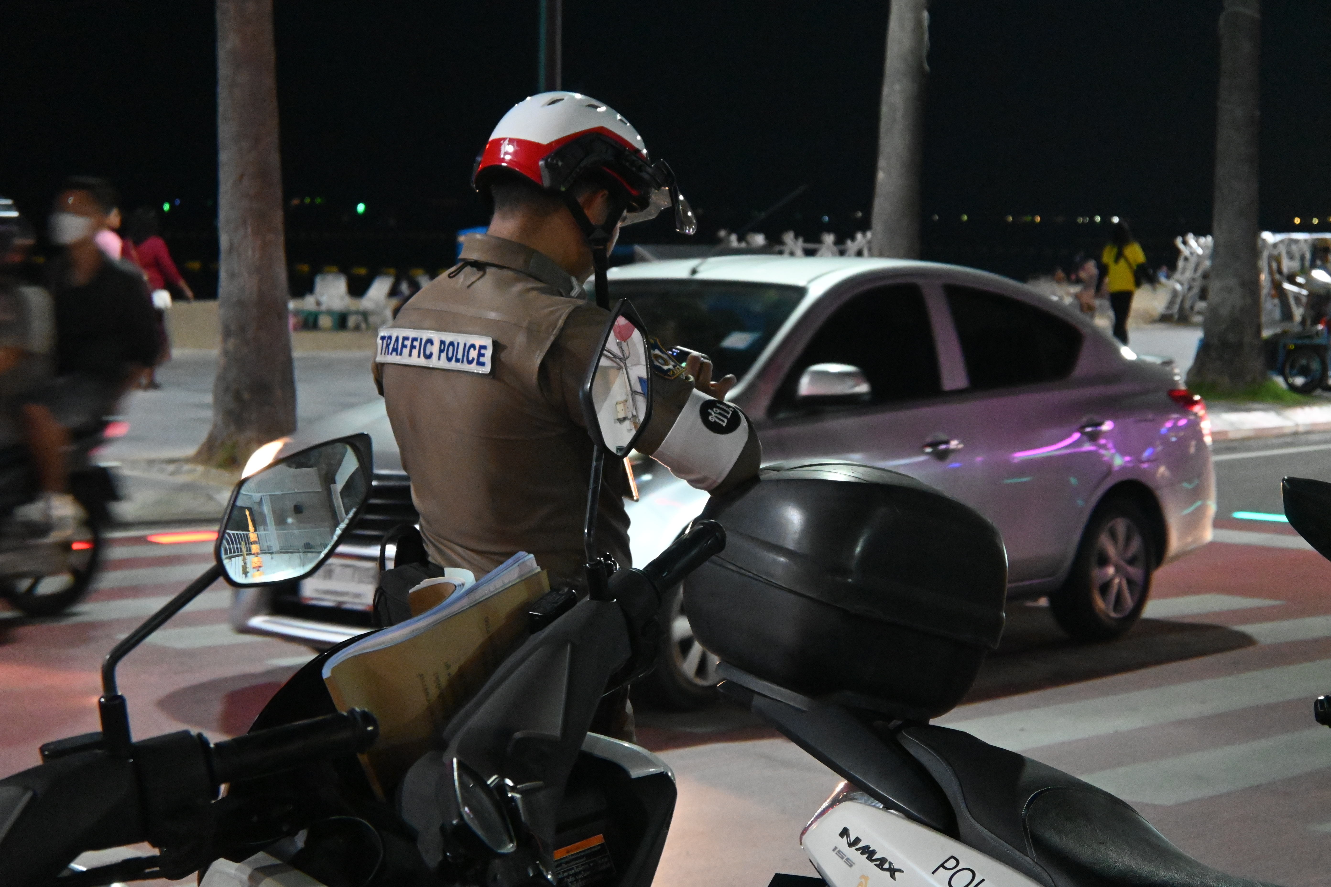 Traffic police officer on motorcycle reviews paperwork beside a pulled-over car at night.