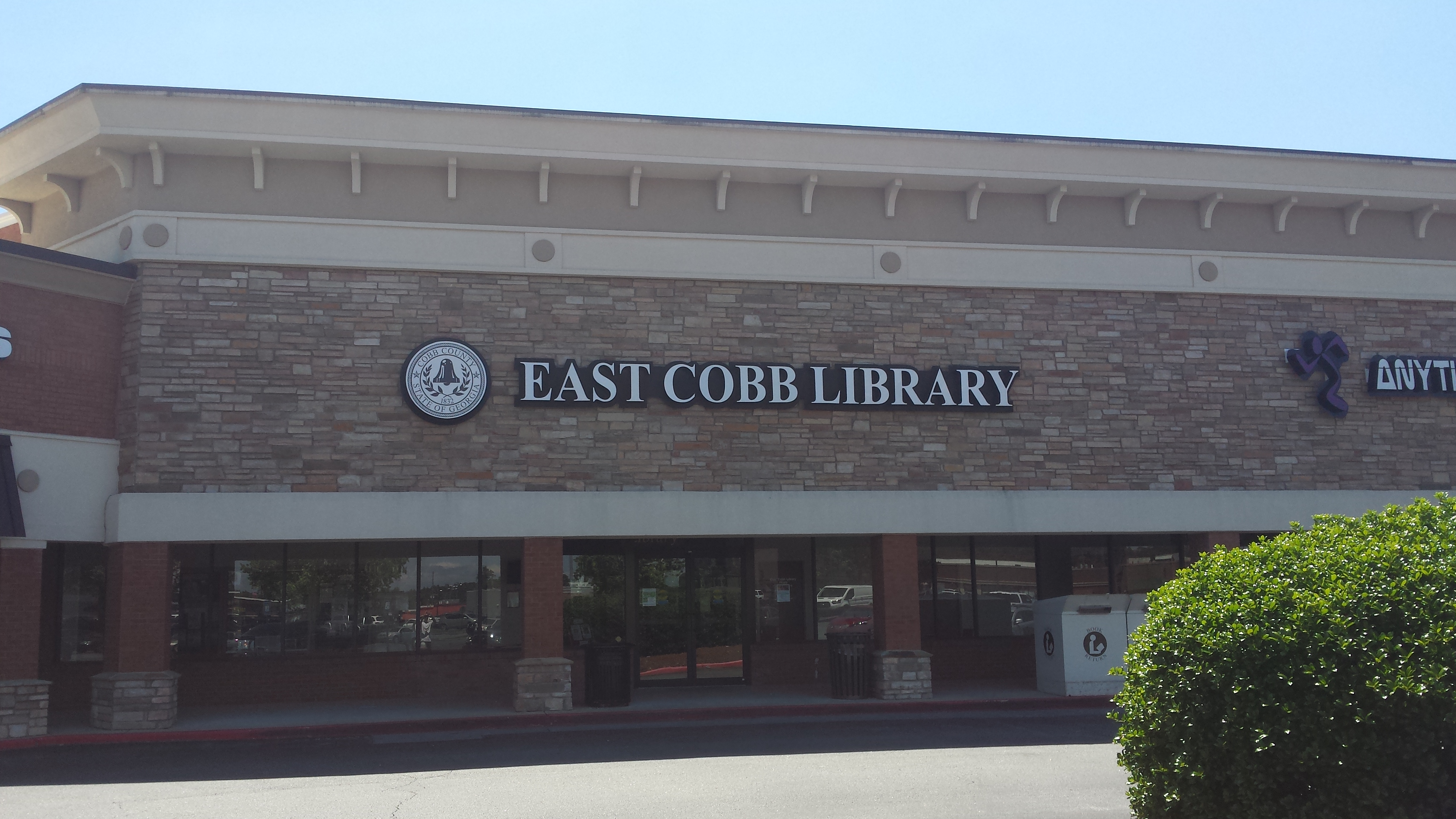 Brick exterior of a library in a strip shopping center with signage above the entrance.