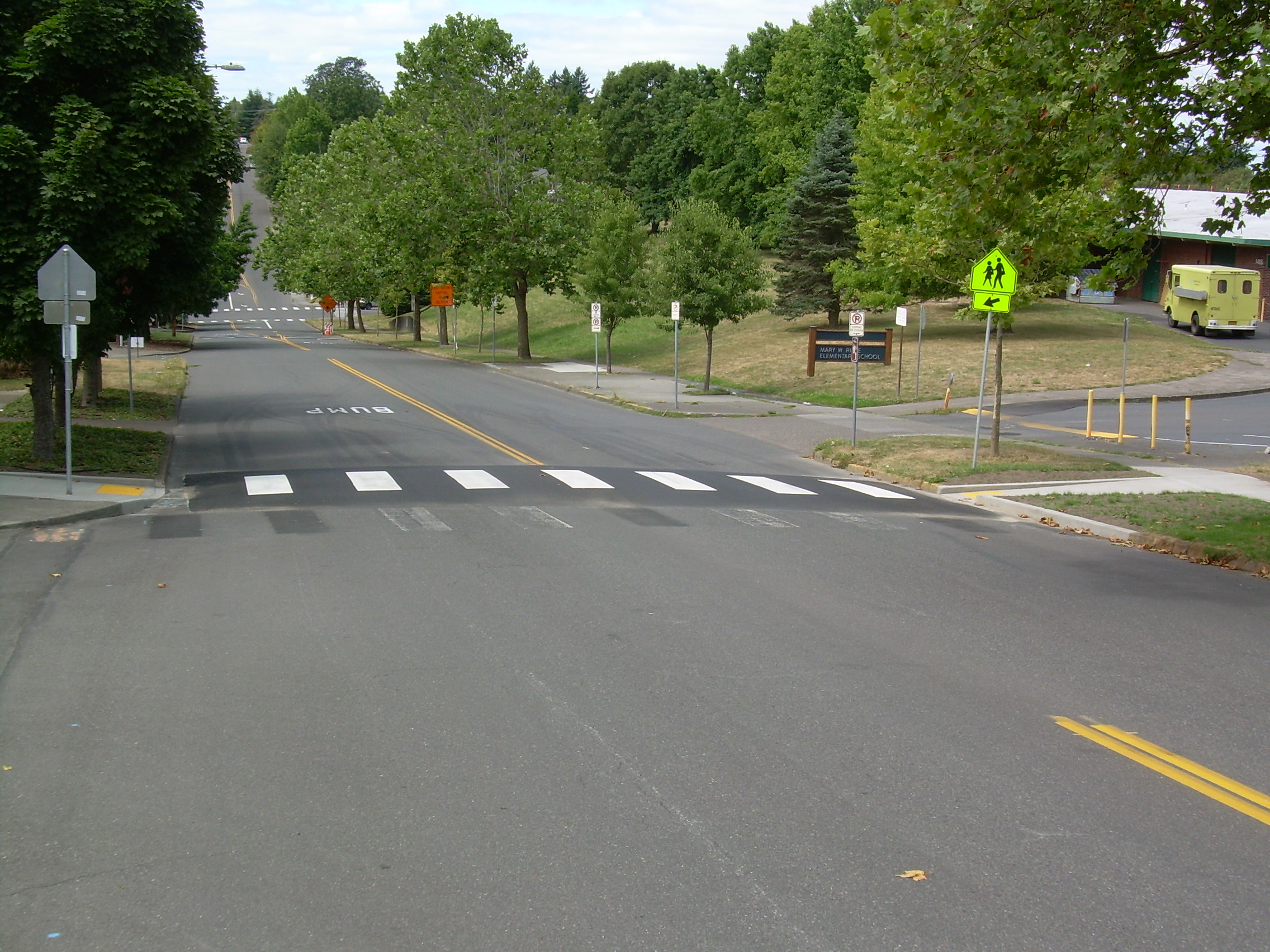 Raised crosswalk with white striping and yellow pedestrian warning signs on a tree-lined street.