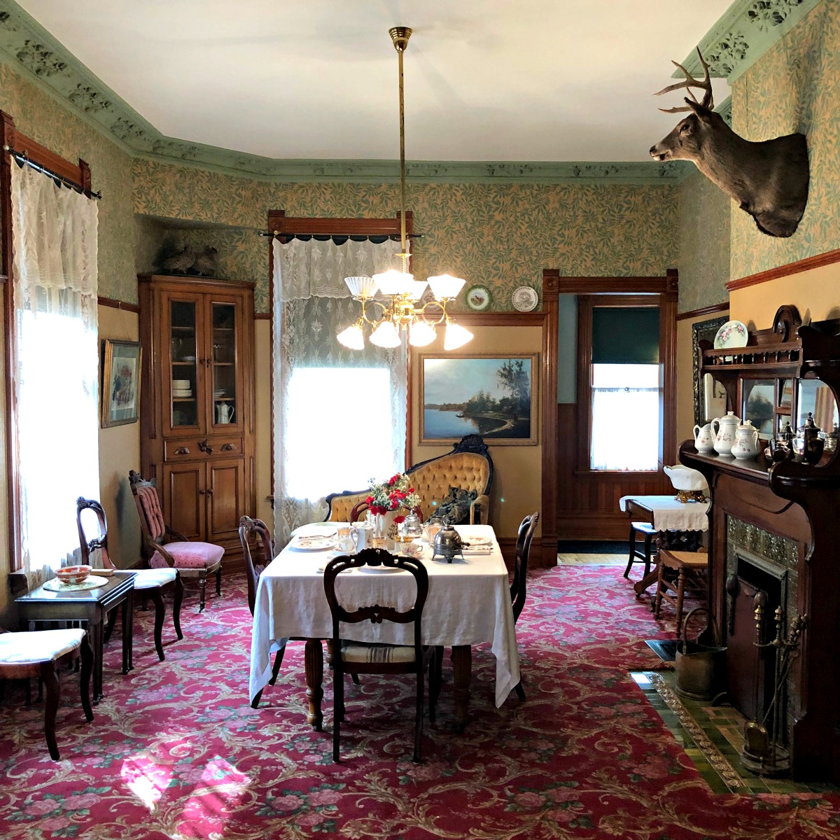 Victorian dining room with period furniture, floral wallpaper, chandelier, and set table.