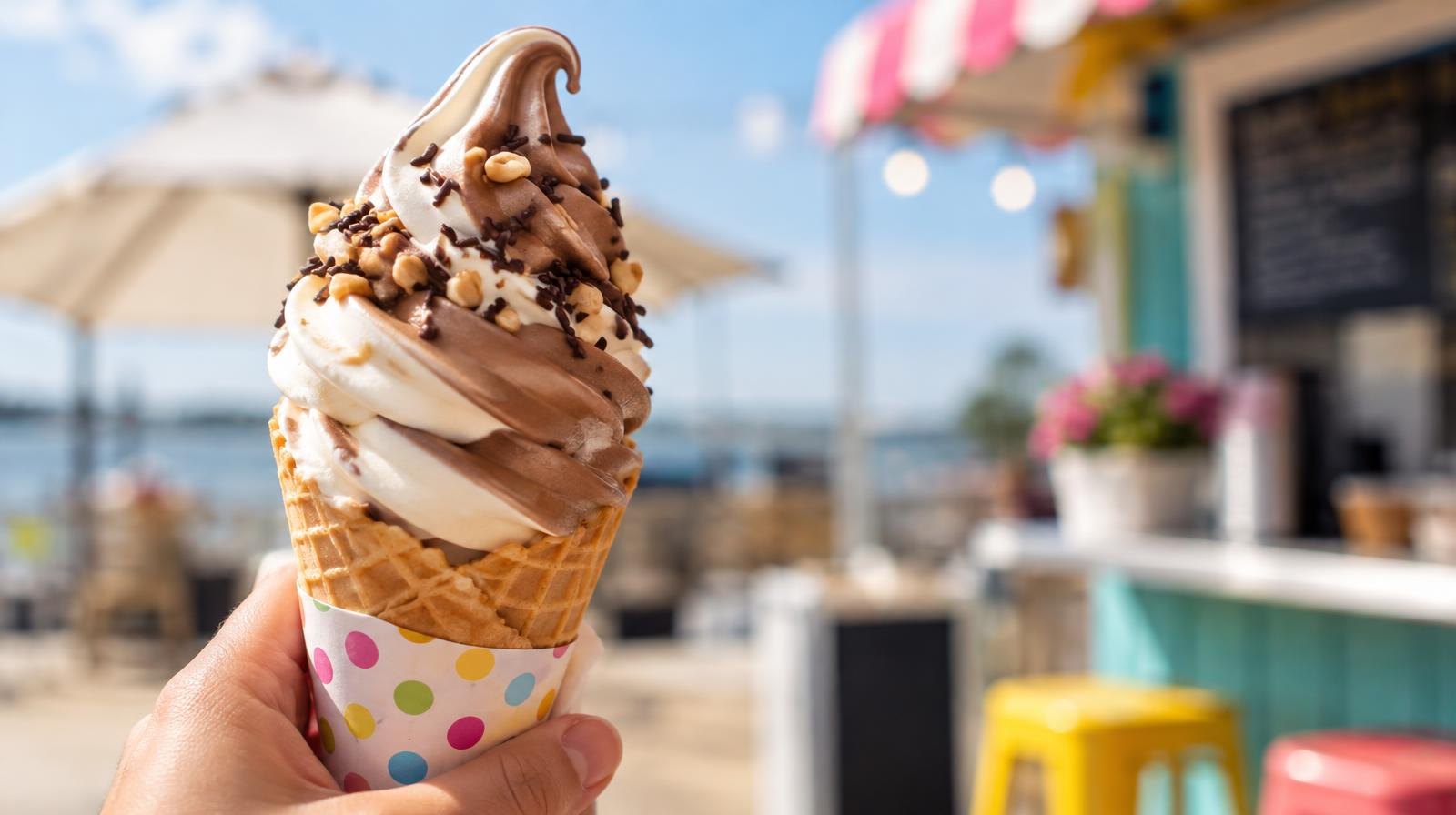 A swirled chocolate and vanilla frozen custard cone held above a paper cup.