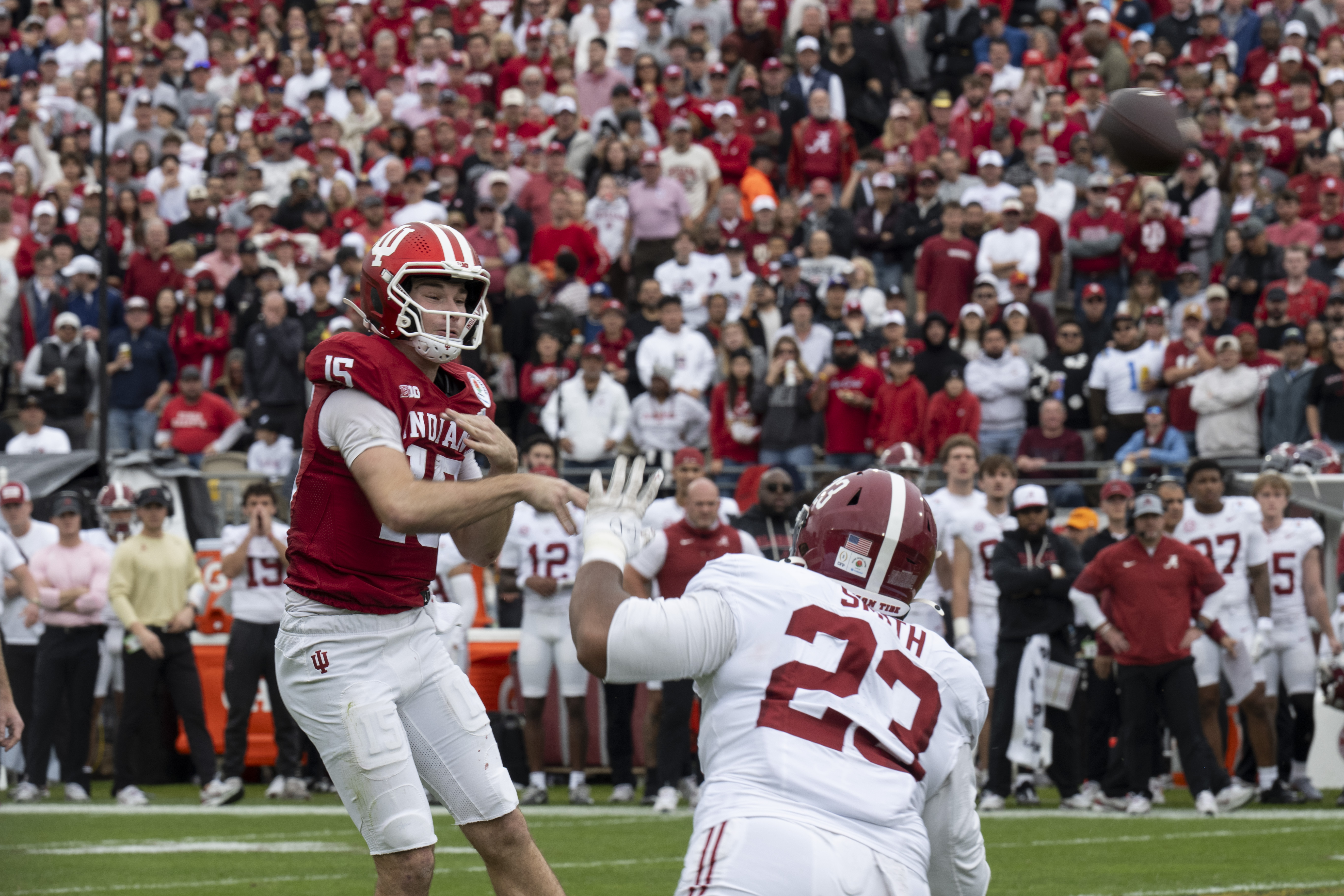 A quarterback in a red uniform throws a pass during a packed college football game.