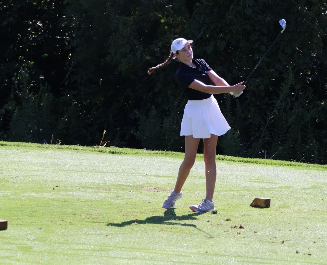 A young female golfer completes a full follow-through swing on a grass fairway.