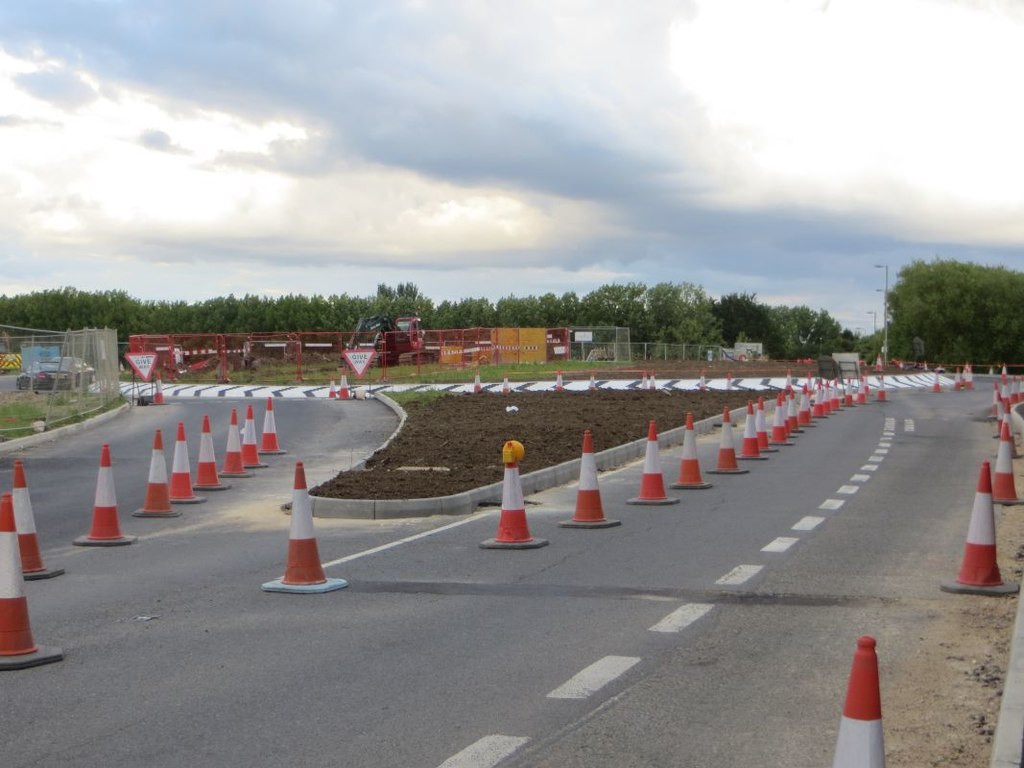 A road lined with orange-and-white traffic cones leading toward a roundabout under construction.