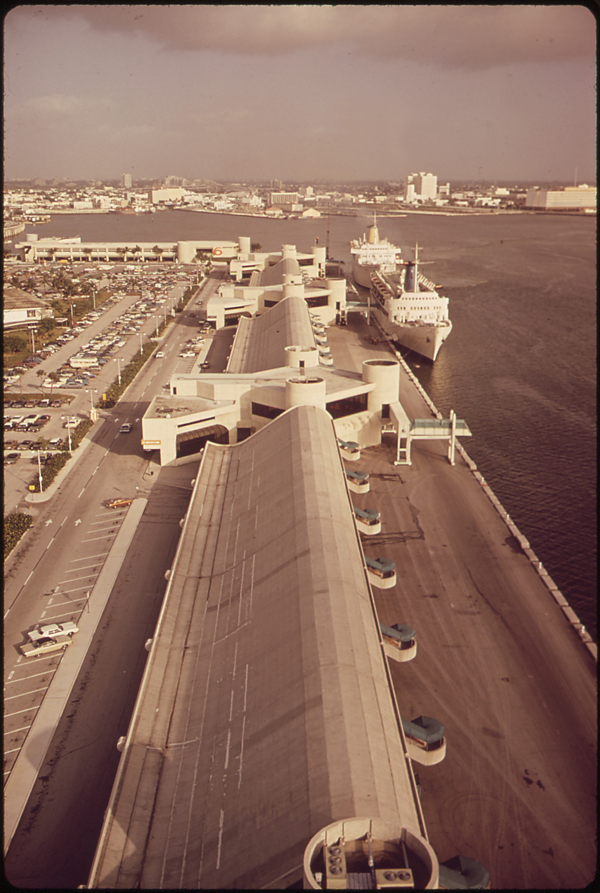 Aerial view of a cruise ship terminal with a large passenger ship docked alongside covered piers.