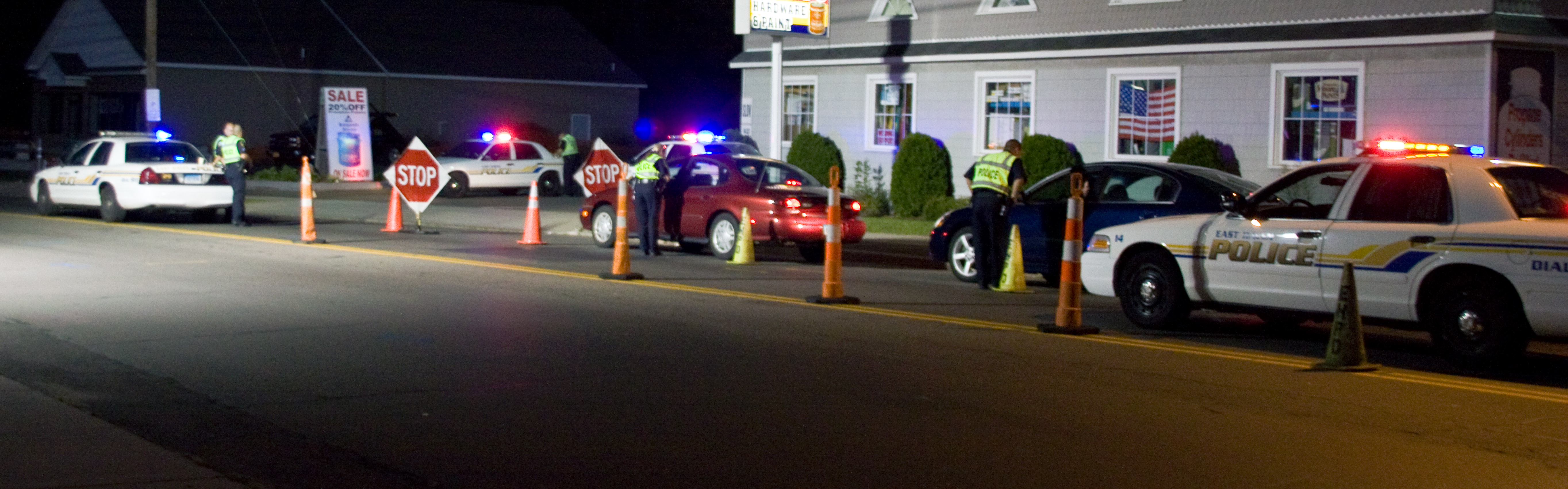Nighttime sobriety checkpoint with police vehicles, cones, and officers in high-visibility vests.