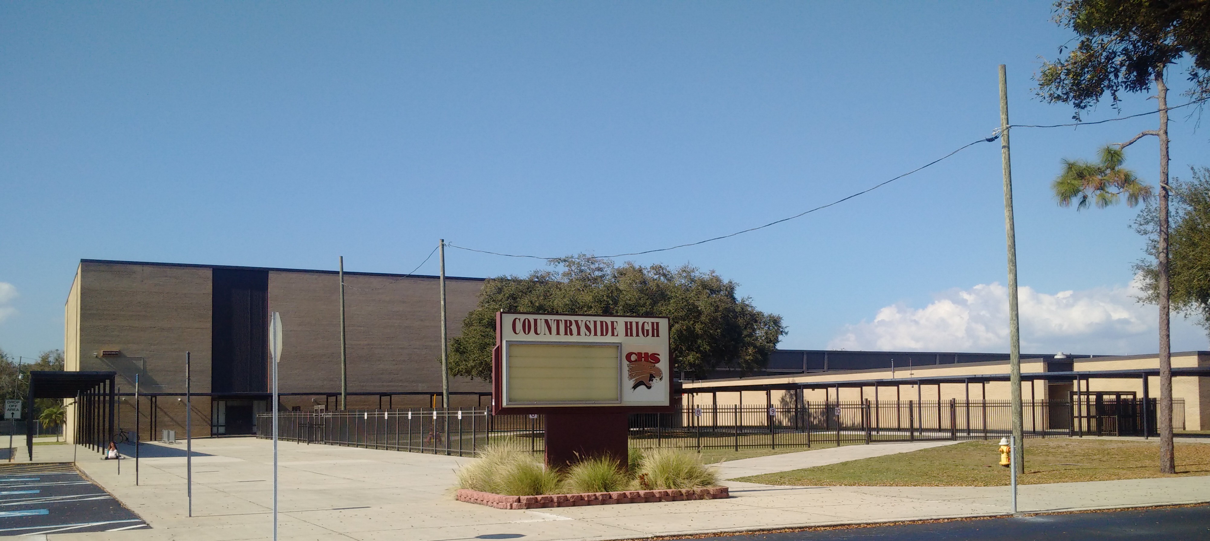 Exterior of a high school with a marquee sign and parking area under a blue sky.