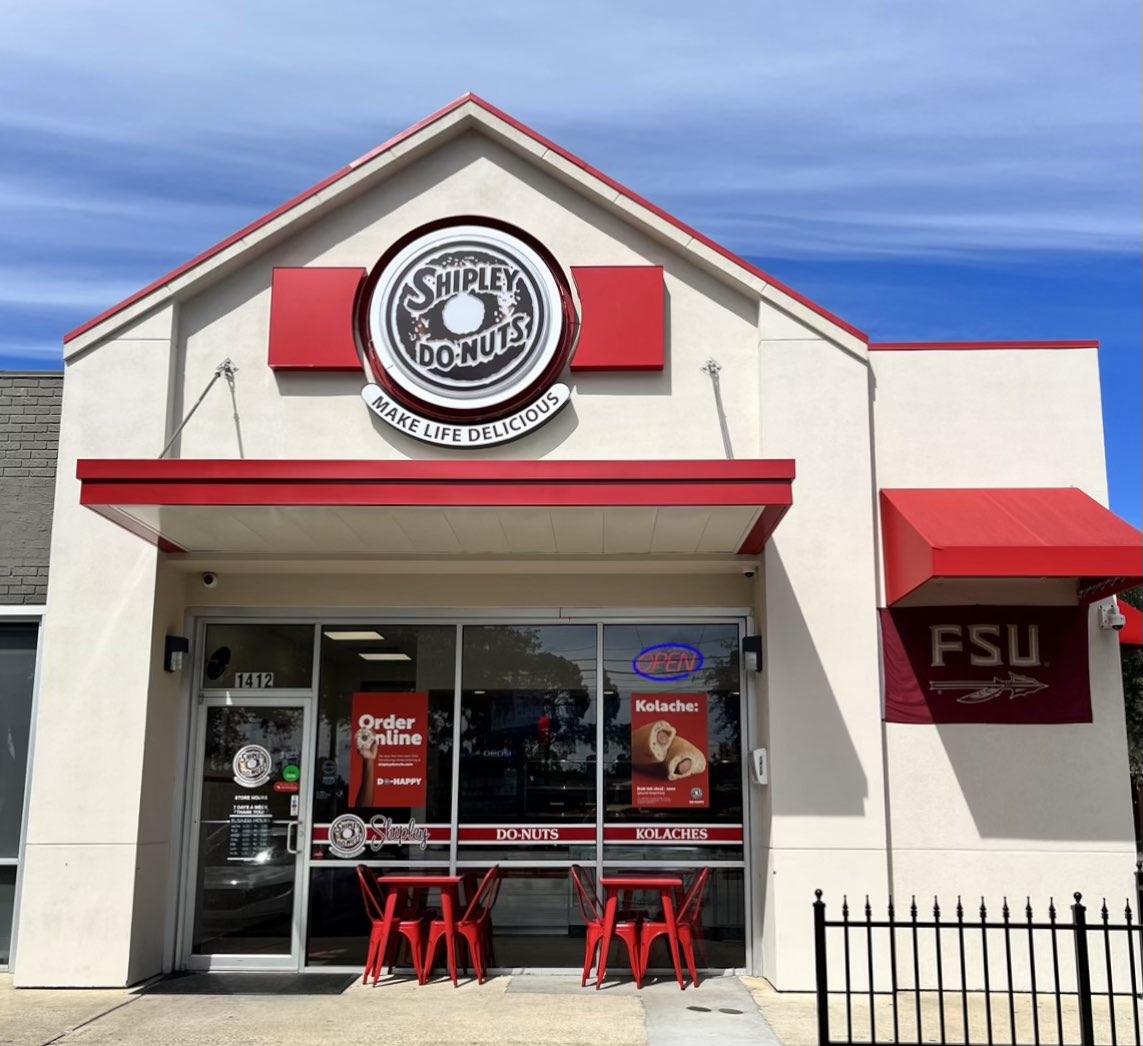 Red and white Shipley Do-Nuts storefront with outdoor seating and window signage.