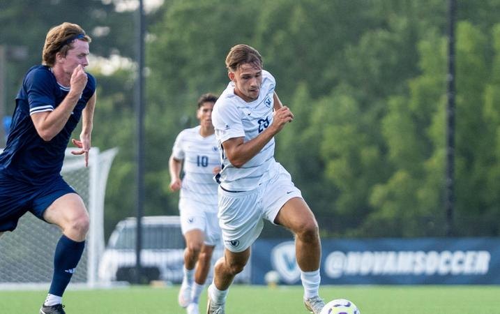 A soccer player in a white uniform dribbles the ball past a defender on a grass field.