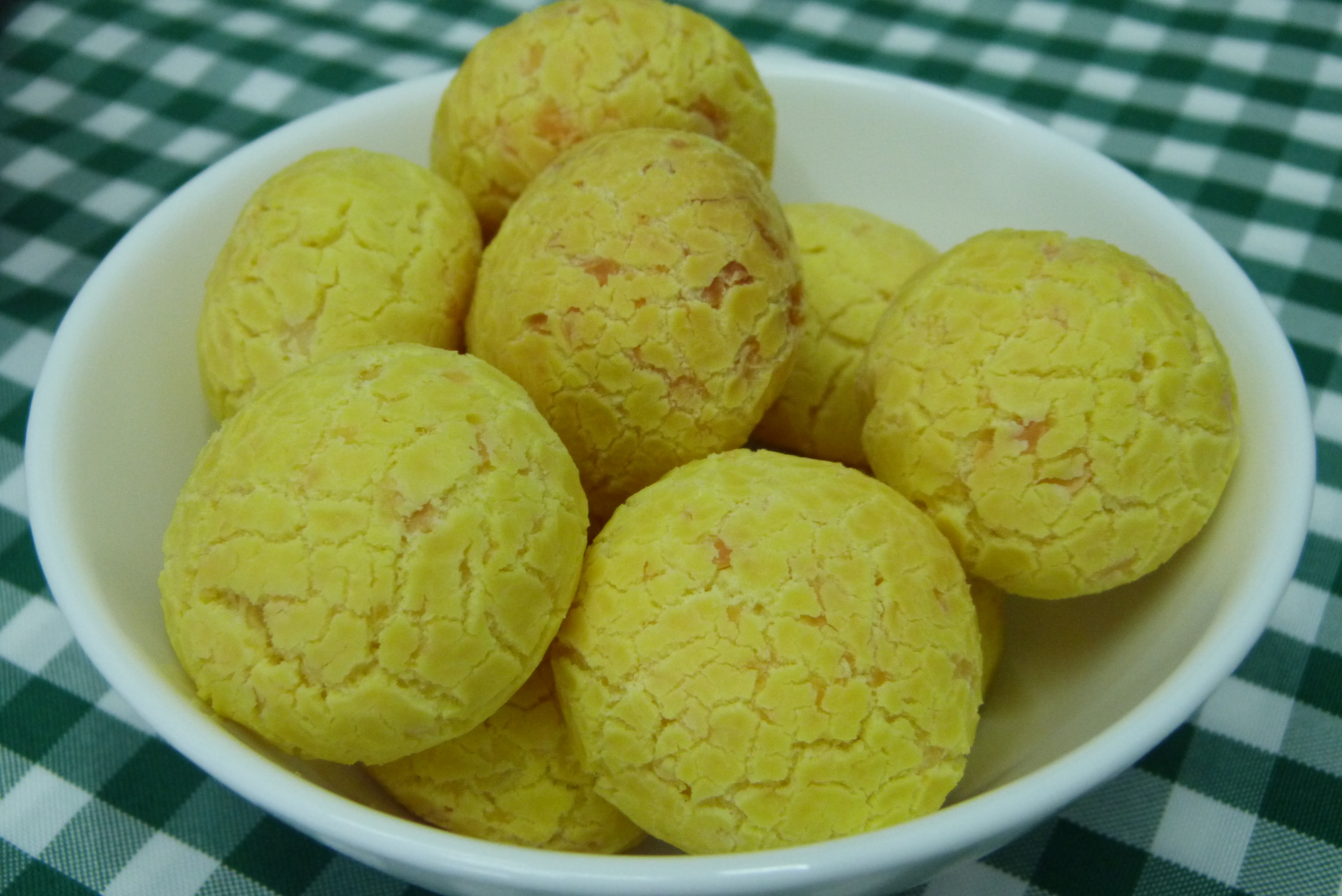 A white bowl filled with round golden-brown Brazilian cheese bread balls.